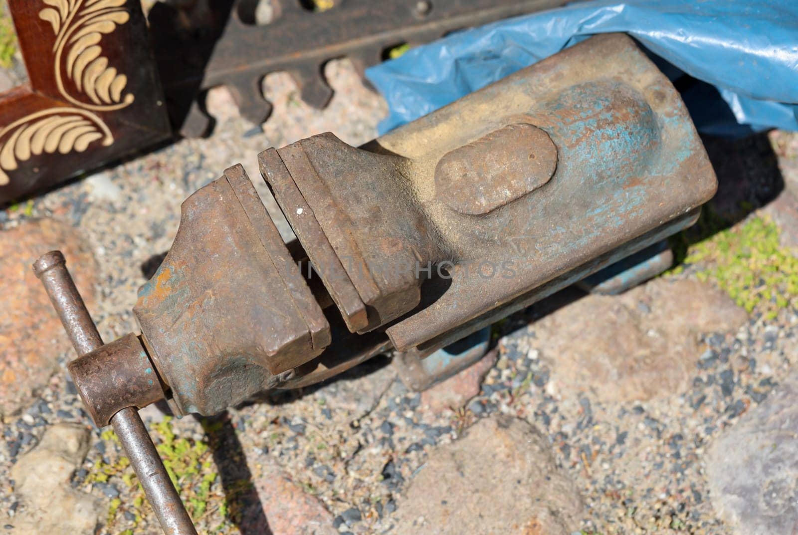 An age large vice stands on a paved floor.