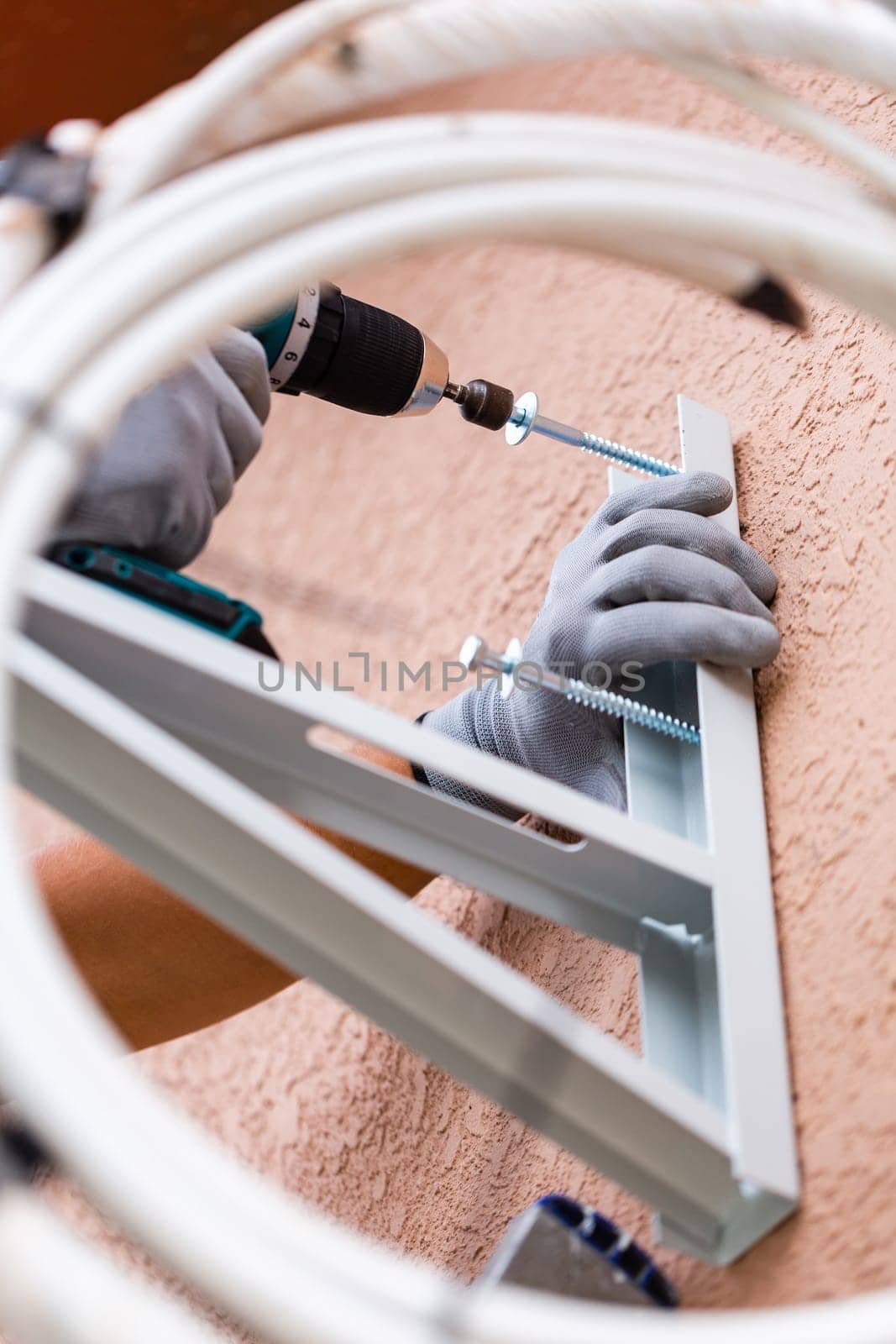Process of installing air conditioning on street. Close up of male worker installing wall mount for outdoor air conditioner unit. Man with drill tightens screws to install air conditioner in wall.