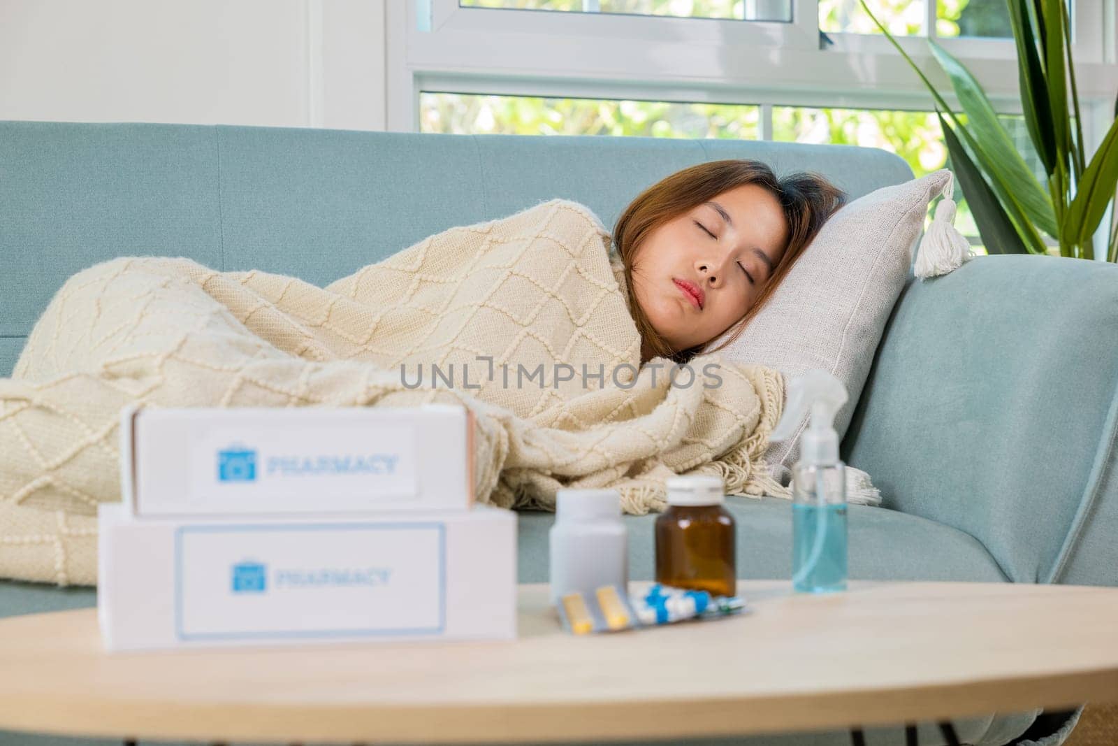 Asian young woman tired sick she sleep and resting on sofa after take medicines pills in living room at home, beautiful female use pharmacy first aid kit box delivery service from hospital, healthcare
