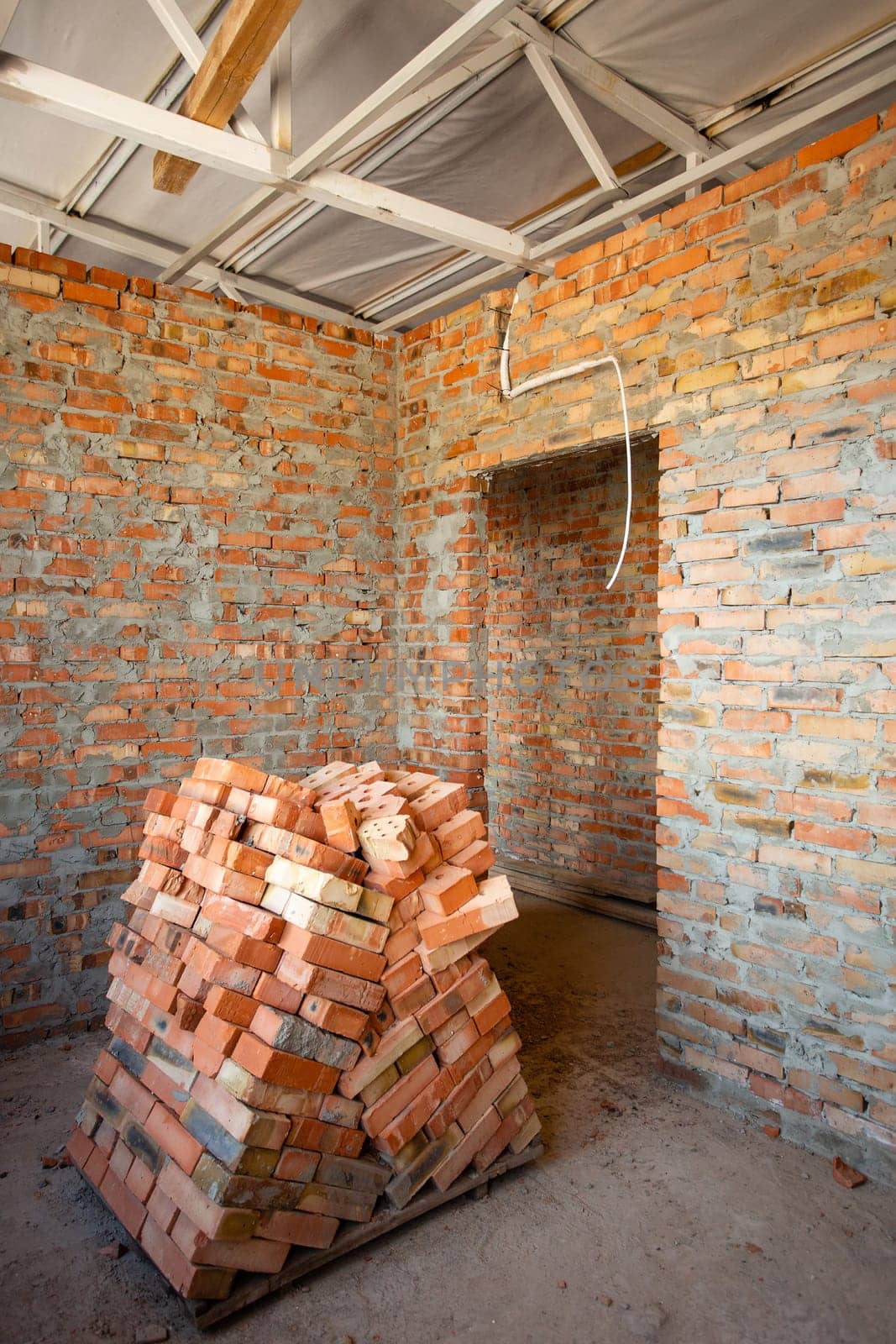 House construction. Start of construction of new apartment with brick walls in new apartment building. Pile of bricks prepared for construction of new house lie in middle ofa room with brick walls.