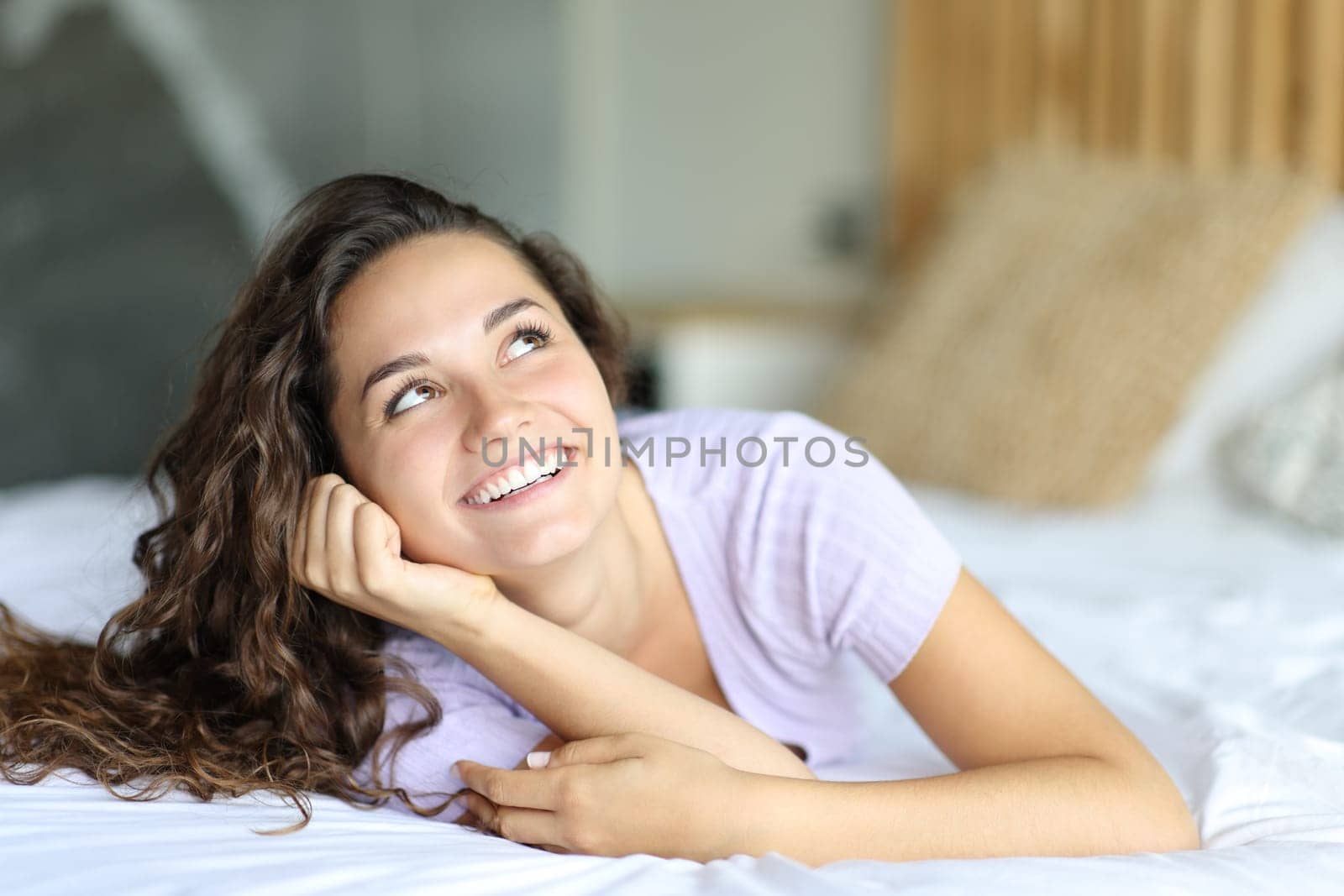 Happy woman looking at side and above lying on the bed