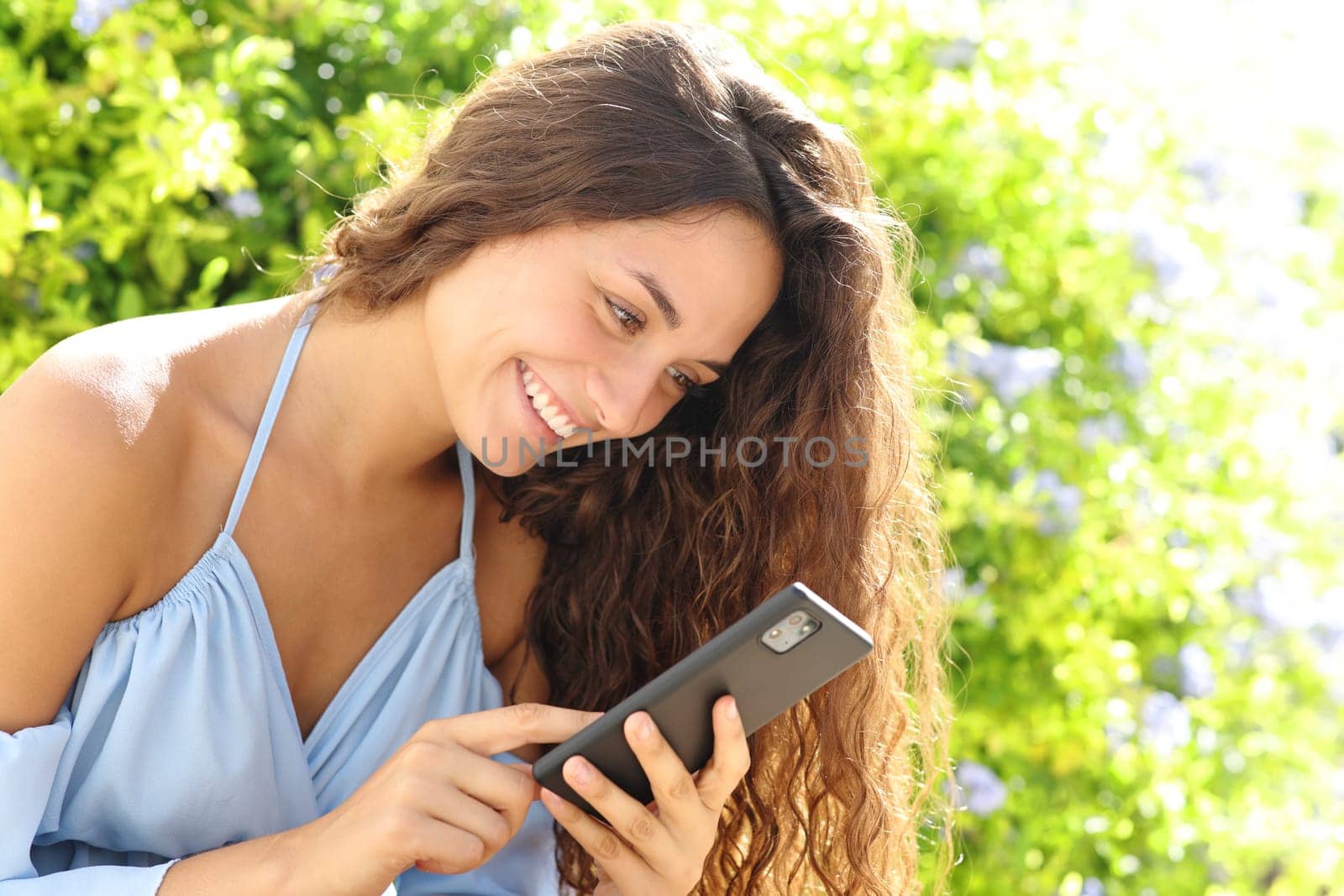 Happy woman in a green garden using smart phone