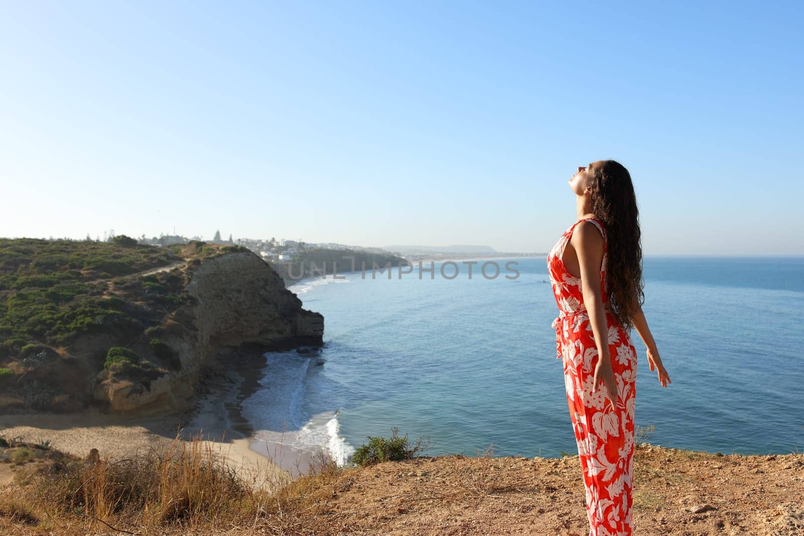Woman in red dress breathing fresh air on a clif on the beach