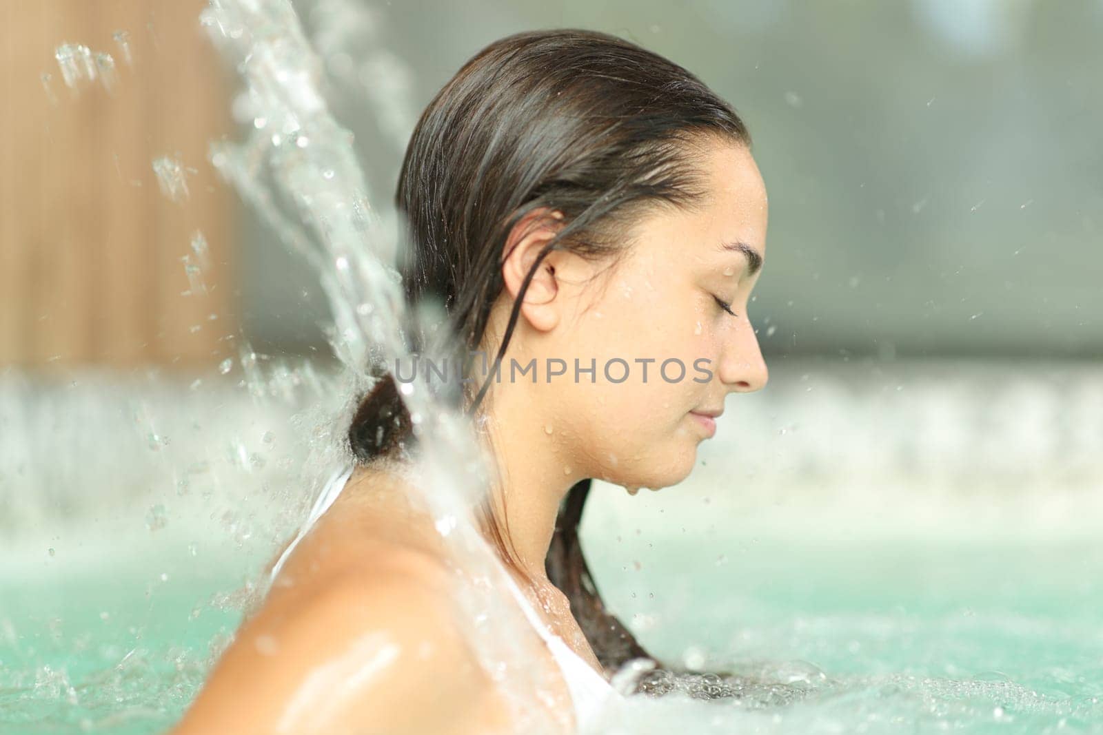 Profile of a woman with closed eyes under water jet in spa pool