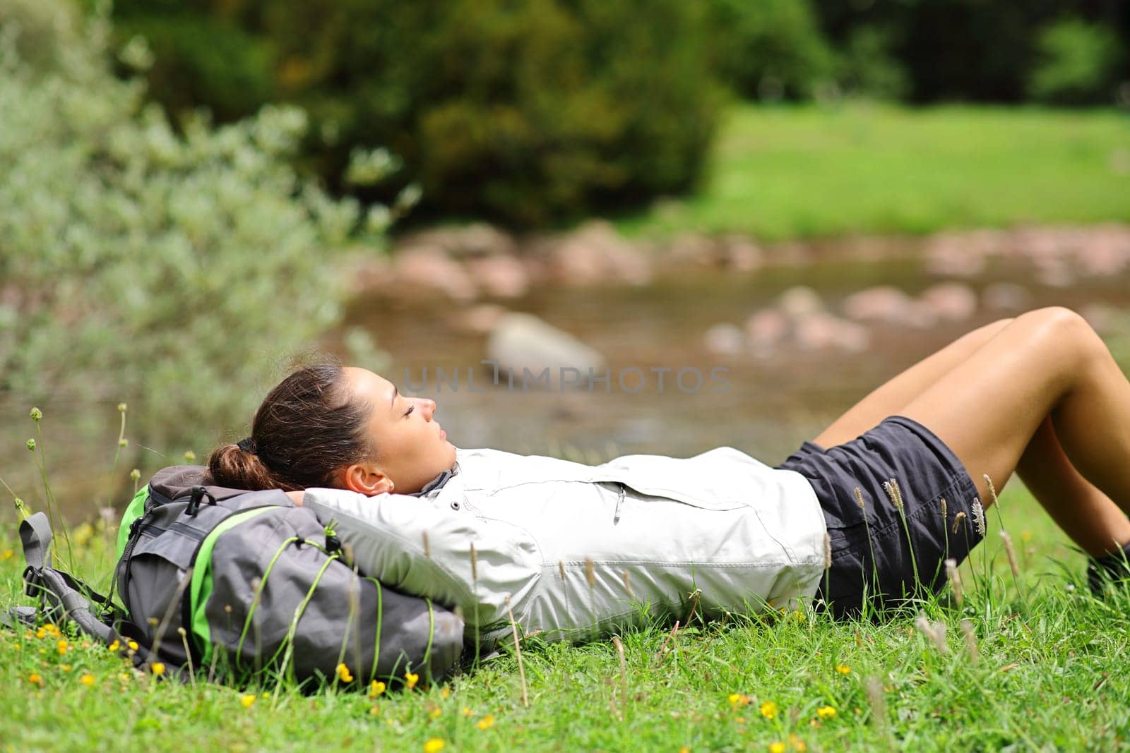 Side view portrait of a trekker resting lying on the grass in a riverside in the mountain
