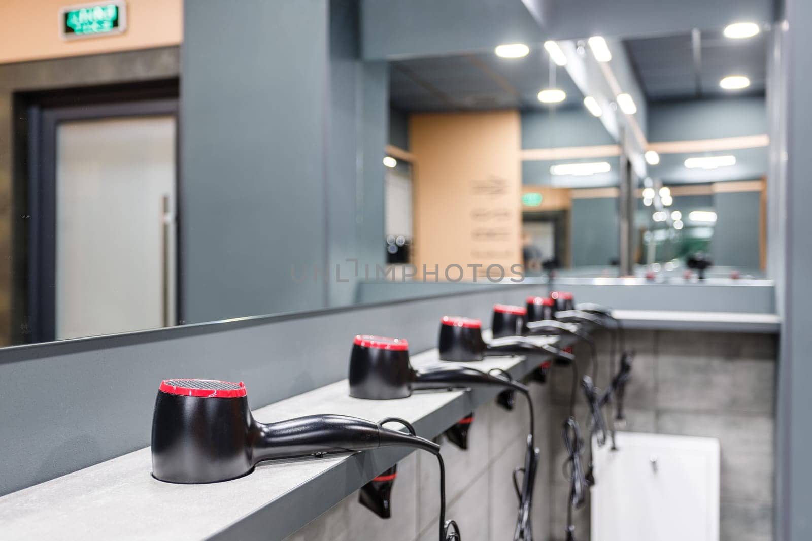Close up of stand in washroom in gym on which are placed in row many hair dryers. Room with mirrors and hairdryers in gym or pool. Concept of services in gym or pool. Selective focus.