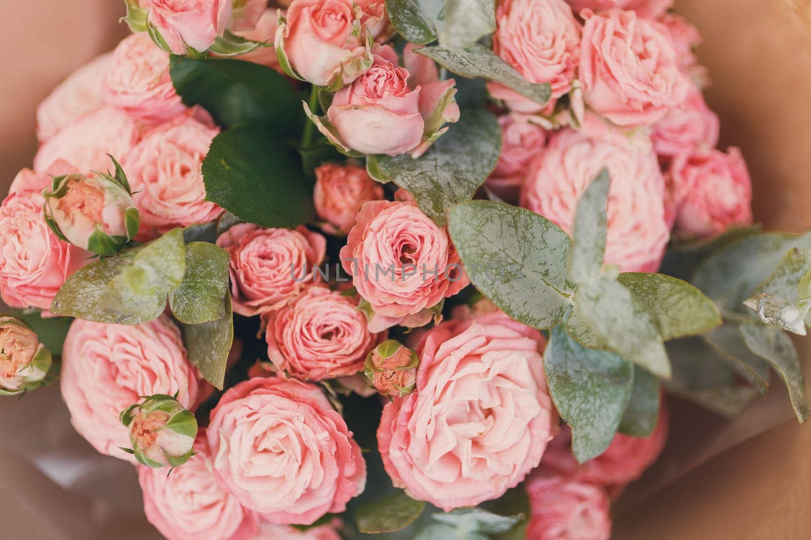 Pink spray roses with sprigs of green eucalyptus stacked together in one festive bouquet. Close up of bouquet of flowers wrapped in brown kraft paper. Concept of flower delivery for any holiday.