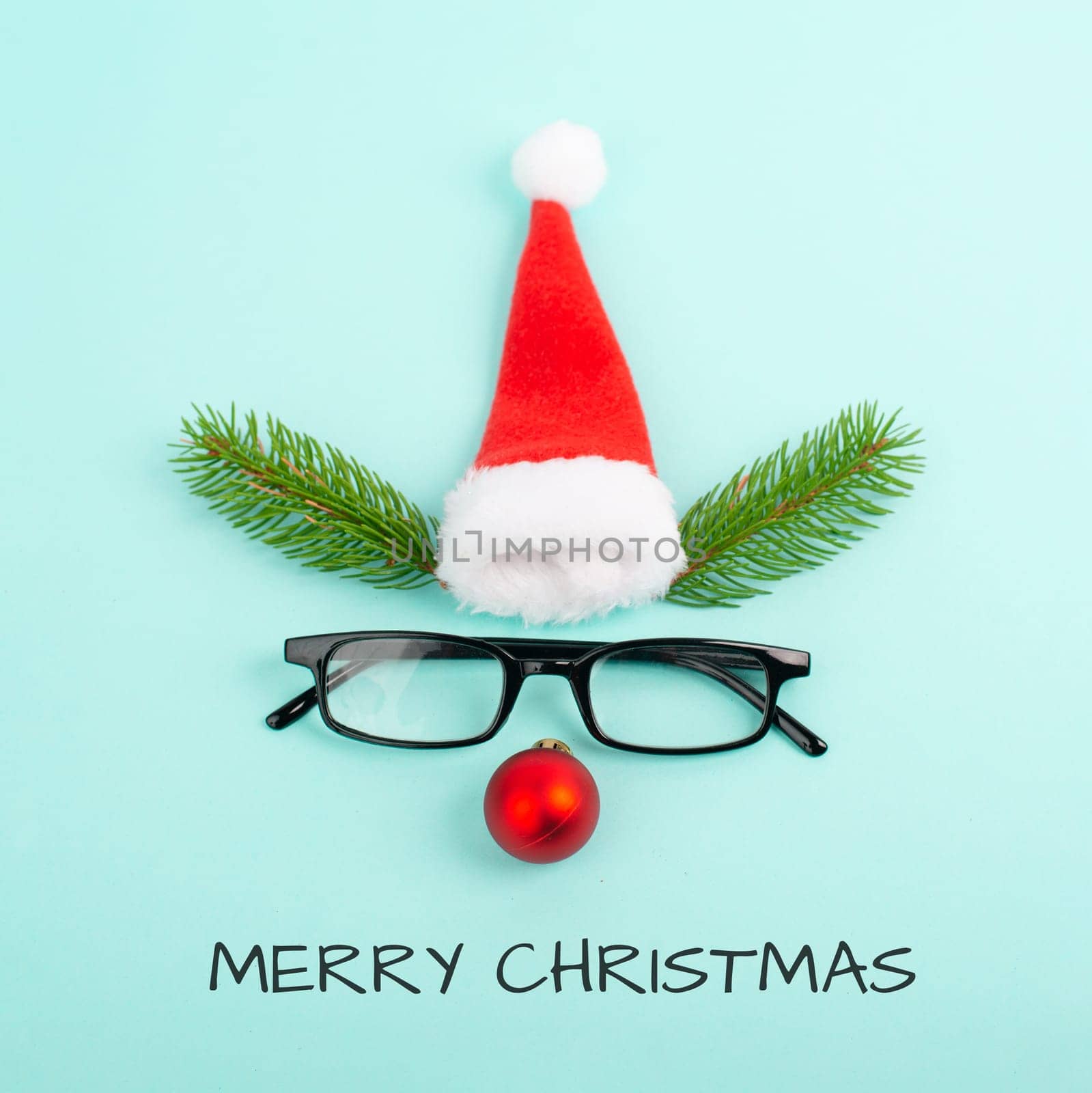 Face of a reindeer with a red bauble nose, fir antlers, a santa claus hat and eyeglasses, merry christmas greeting card