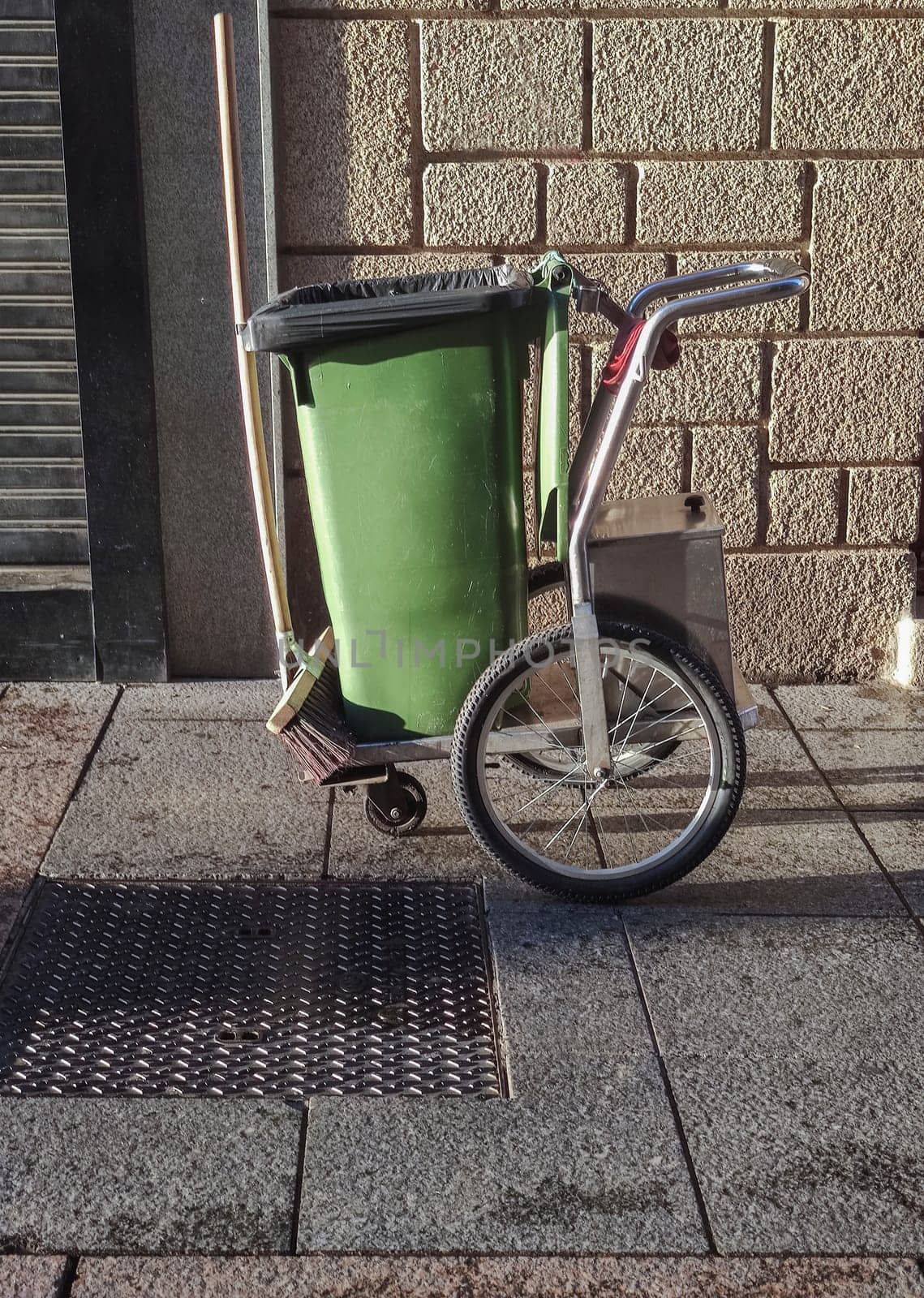 Street sweeper cart with green dumpster and sweep. Downtown background