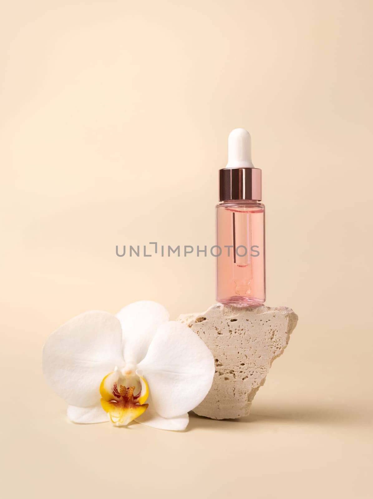 Dropper Bottle on stone near white orchid flowers on light yellow, close up, mockup. Skincare beauty product, essential oil or serum. Exotic cosmetics, pastel minimal composition..