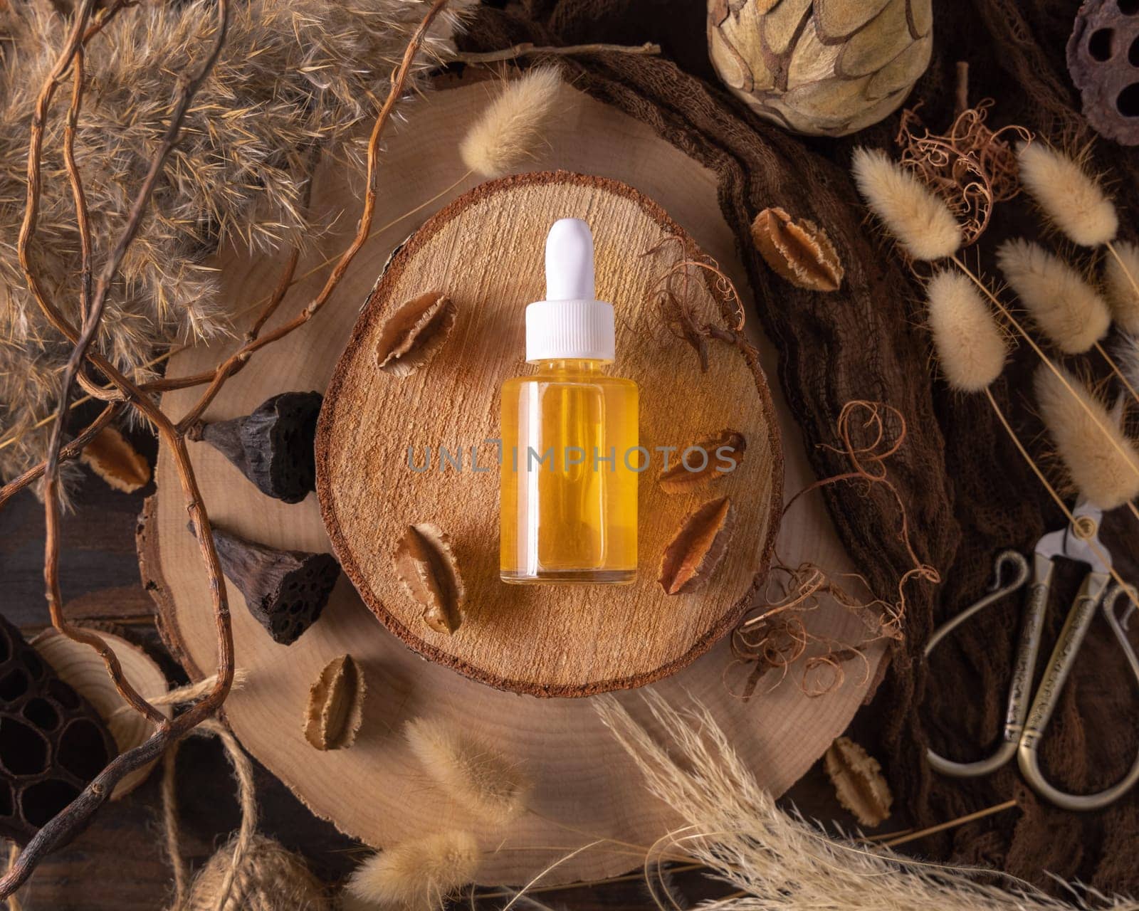 Dropper bottle with yellow liquid on wood near natural boho decorations top view, cosmetic packaging mockup. Skincare beauty product, serum or essence. Bohemian eco friendly flat lay with dried leaves.