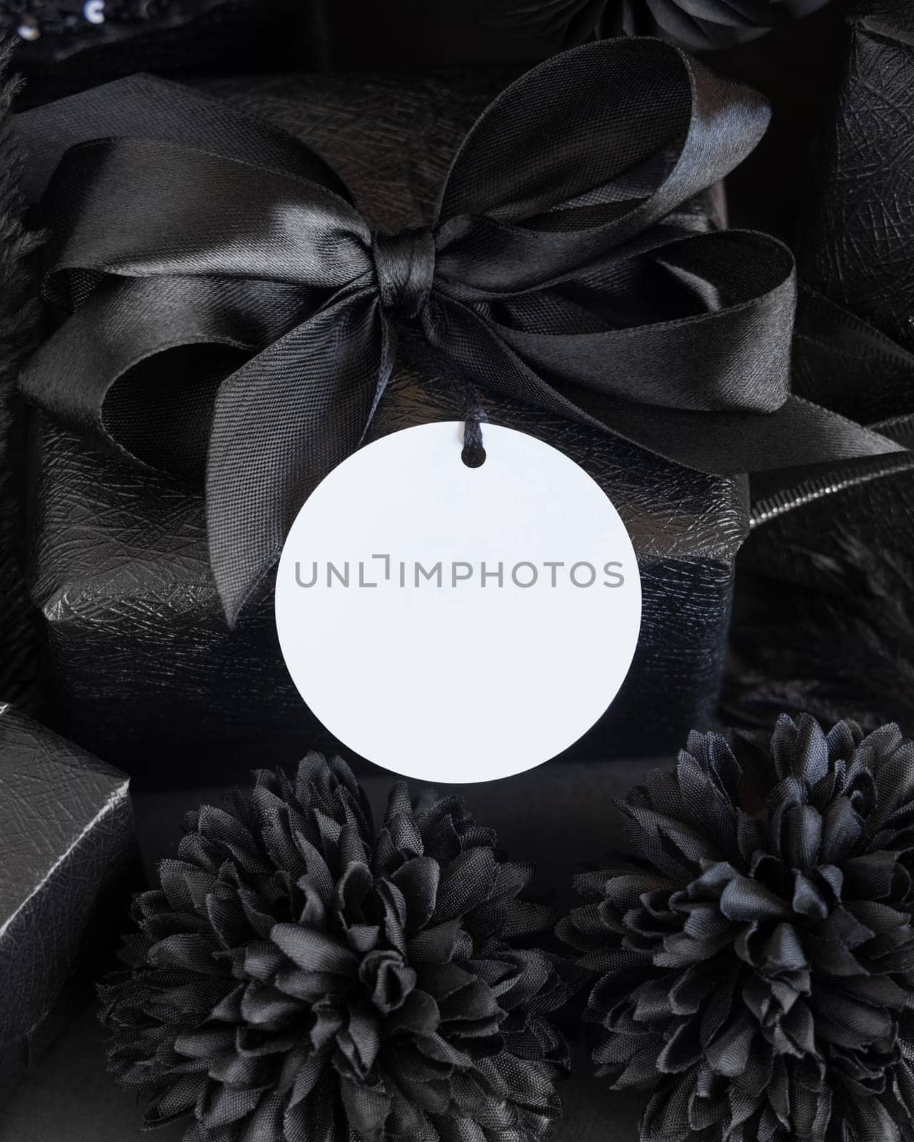 Wrapped Gift Boxes with black paper flowers and decorations and round gift tag, mockup, copy space. Dark composition with blank label card for Birthday, Anniversary or black party present