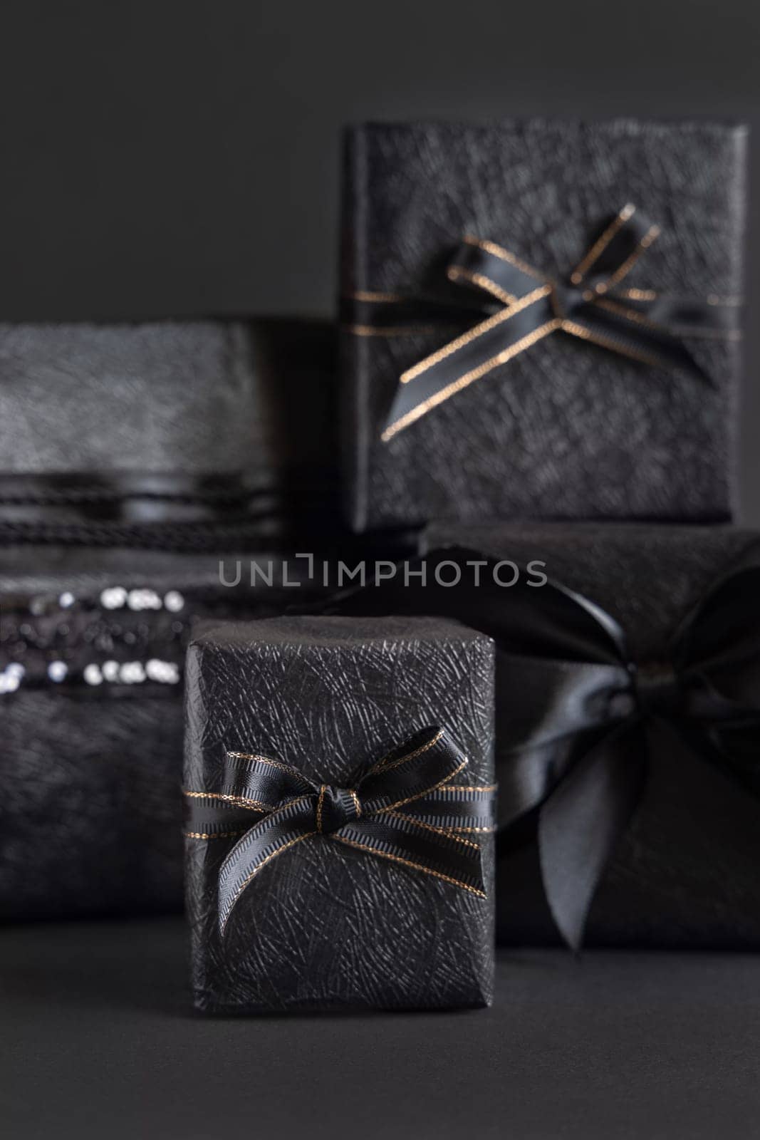 Black Gift Boxes with a ribbon bow on black close up. Wrapped presents for Dark themed Party, Christmas, Birthday, Anniversary. Black Friday concept. Monochrome composition