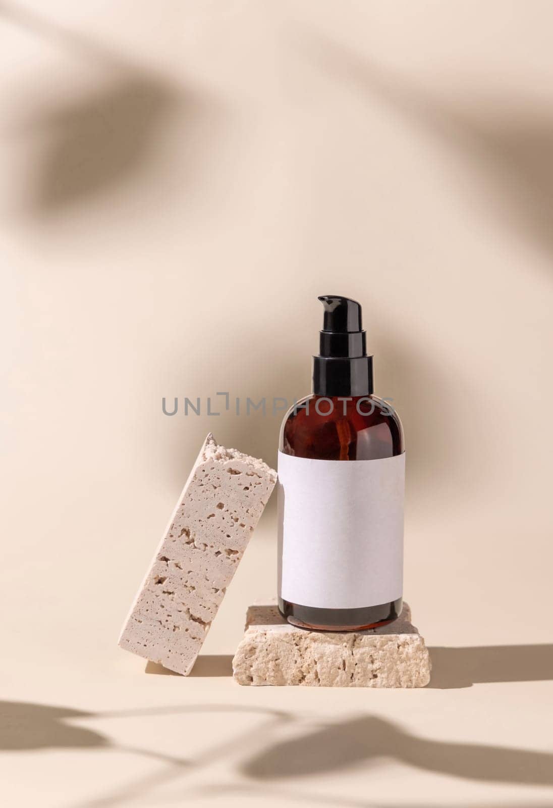 Brown Glass cosmetic one pump bottle on travertine stone on light beige, hard shadows, close up, label mockup. Skincare beauty product, lotion or essence. Natural cosmetics.