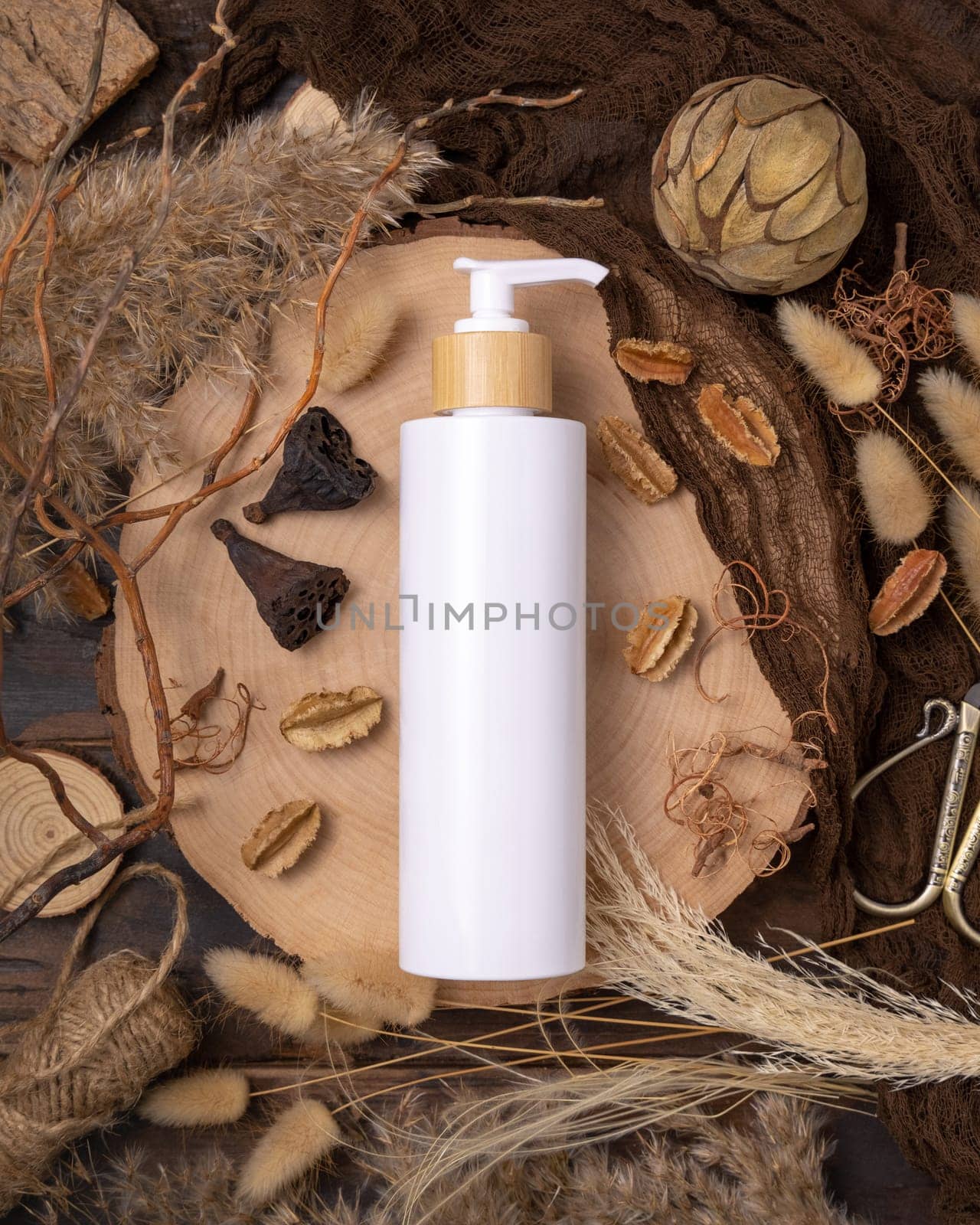 Refillable white one pump bottle on wood near natural boho decorations top view, label mockup. Skincare beauty product, lotion or essence. Bohemian eco friendly cosmetics flat lay with dried leaves.