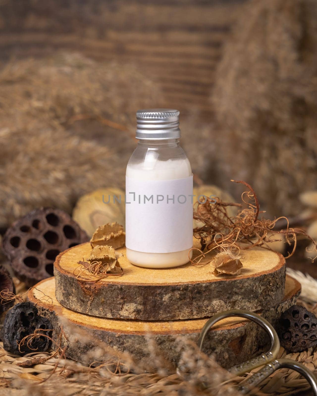 Cosmetic bottle with blank label on wood near natural decorations close up, package mockup. Eco friendly skincare product, lotion or cream. Bohemian composition with dried leaves and flowers.