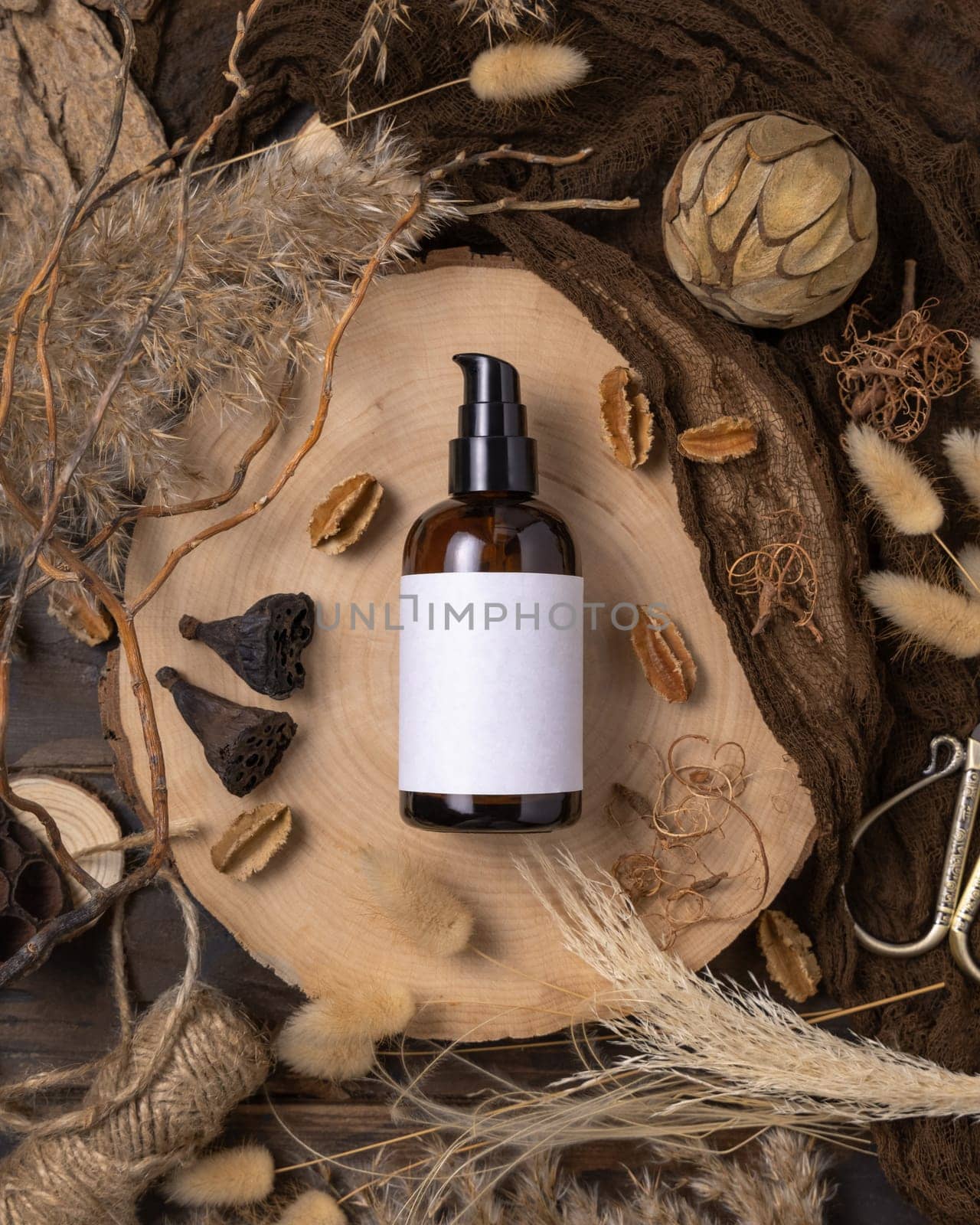 Glass one pump bottle on wood near natural boho decorations top view, label mockup. Skincare beauty product, lotion or essence. Bohemian eco friendly cosmetics flat lay with dried leaves.