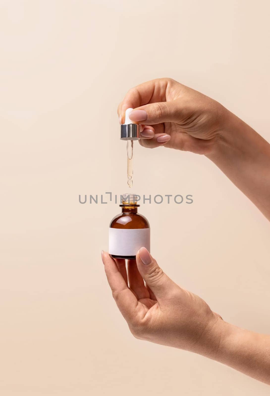 Hands holding pipette and opened dropper bottle with blank label over light beige, close up, mockup. Natural cosmetic, serum or essence. Everyday woman skincare routine.