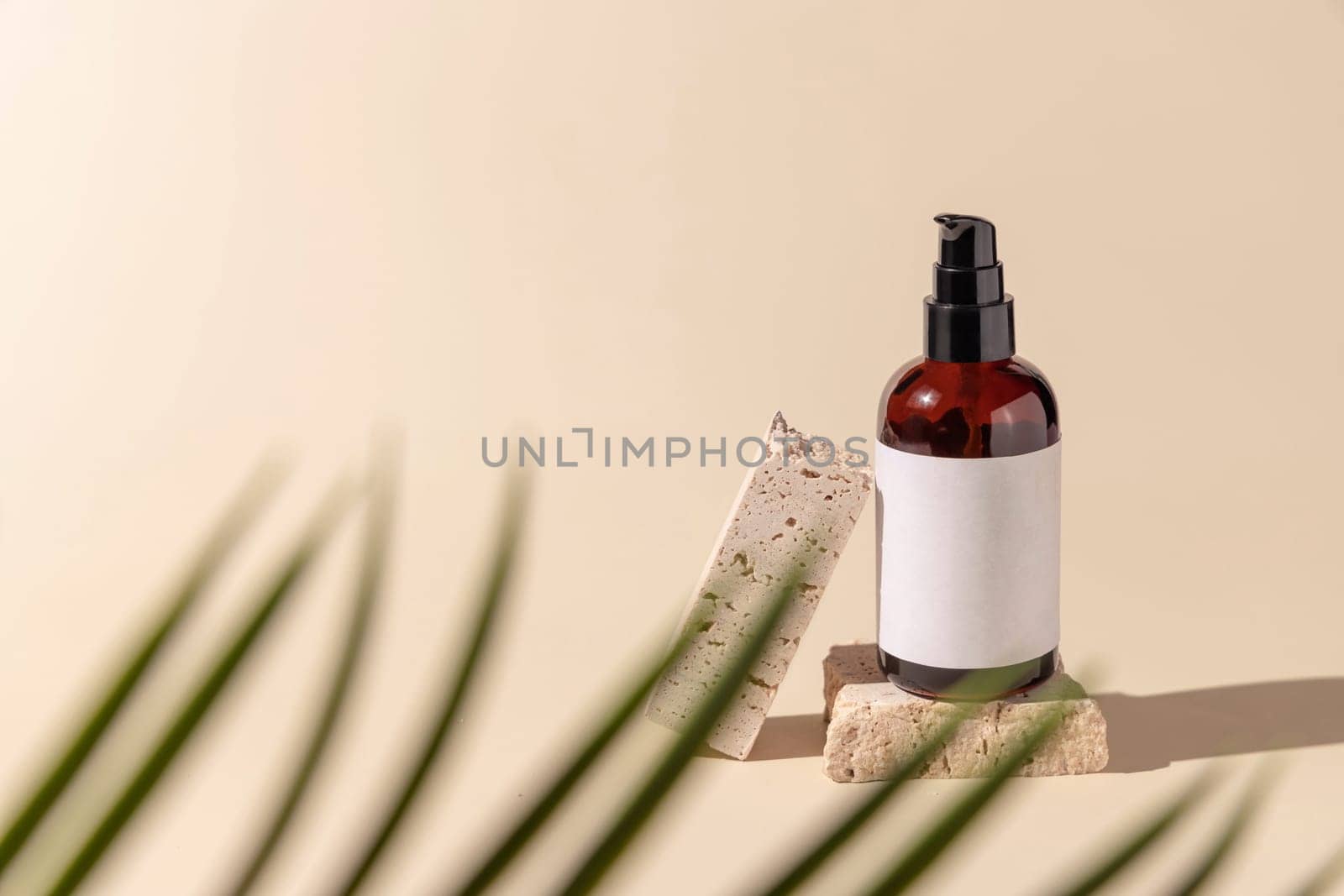 Glass cosmetic one pump bottle on stone on light beige with a palm leaf, close up, label mockup. Skincare beauty product, lotion or essence. Natural cosmetics.