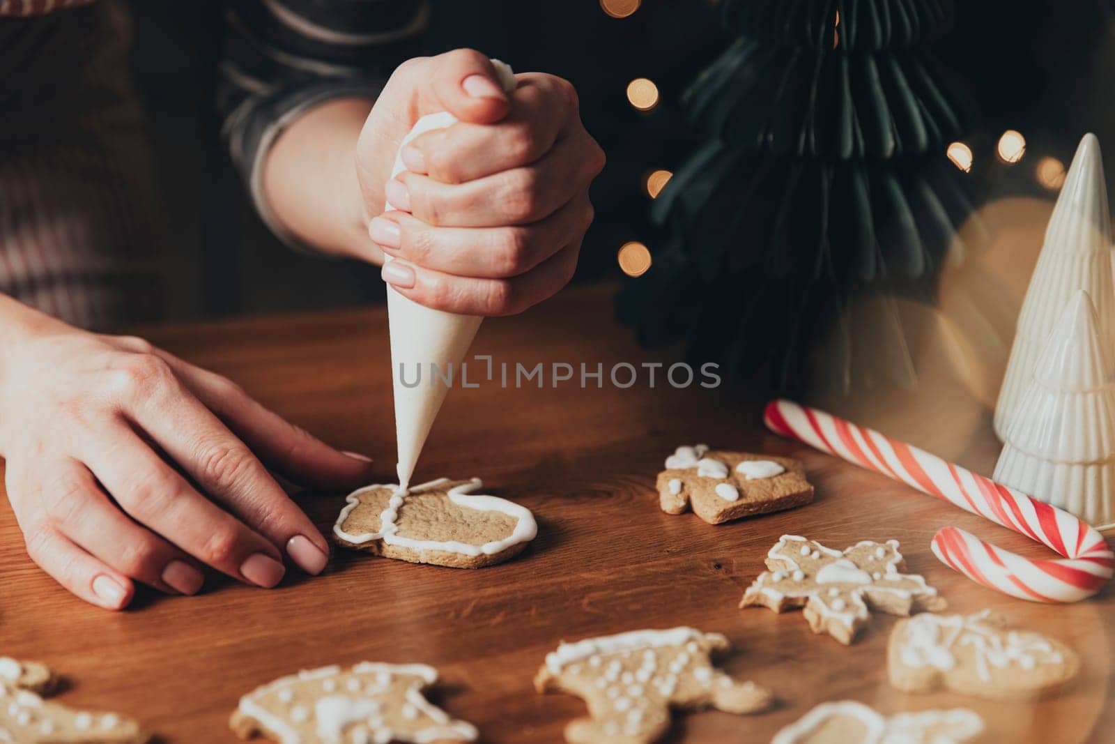 Christmas, New Year food preparation. Xmas gingerbread cooking, making and decorating freshly baked cookies. Closeup on cropped shot with woman hands holding icing and mastic, decorating cookies