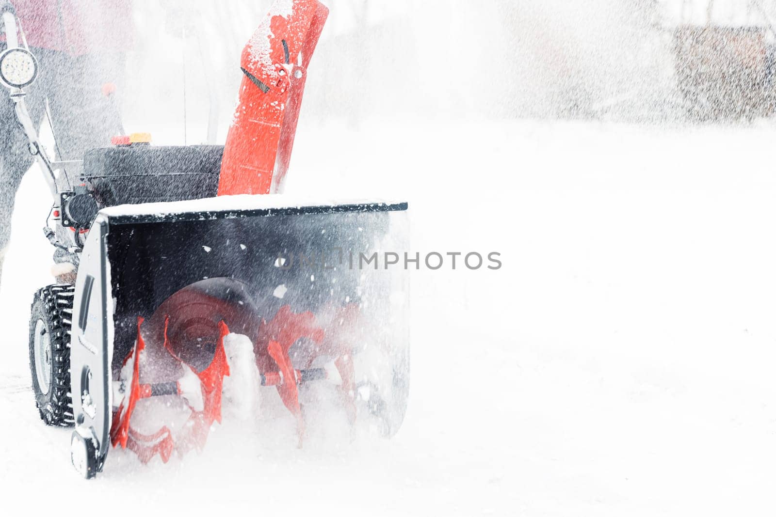 Detail closeup of portable red snow blower powered by gasoline in action. Man outdoor using snowblower machine after snowstorm, snowfall for clearing, removing snow. Snow removal, thrower assistant