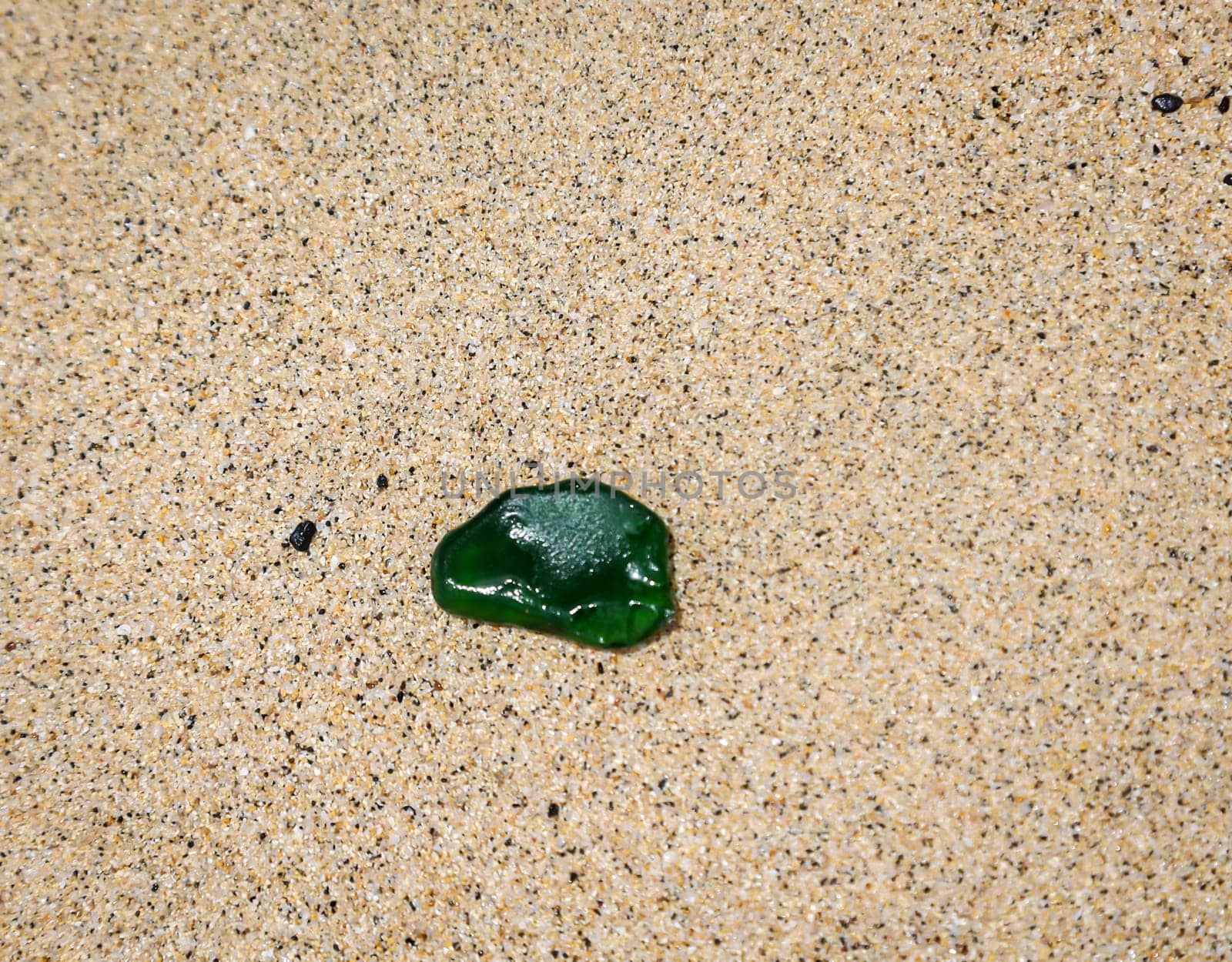 A green glass pane on the beach. A so-called sea glass.