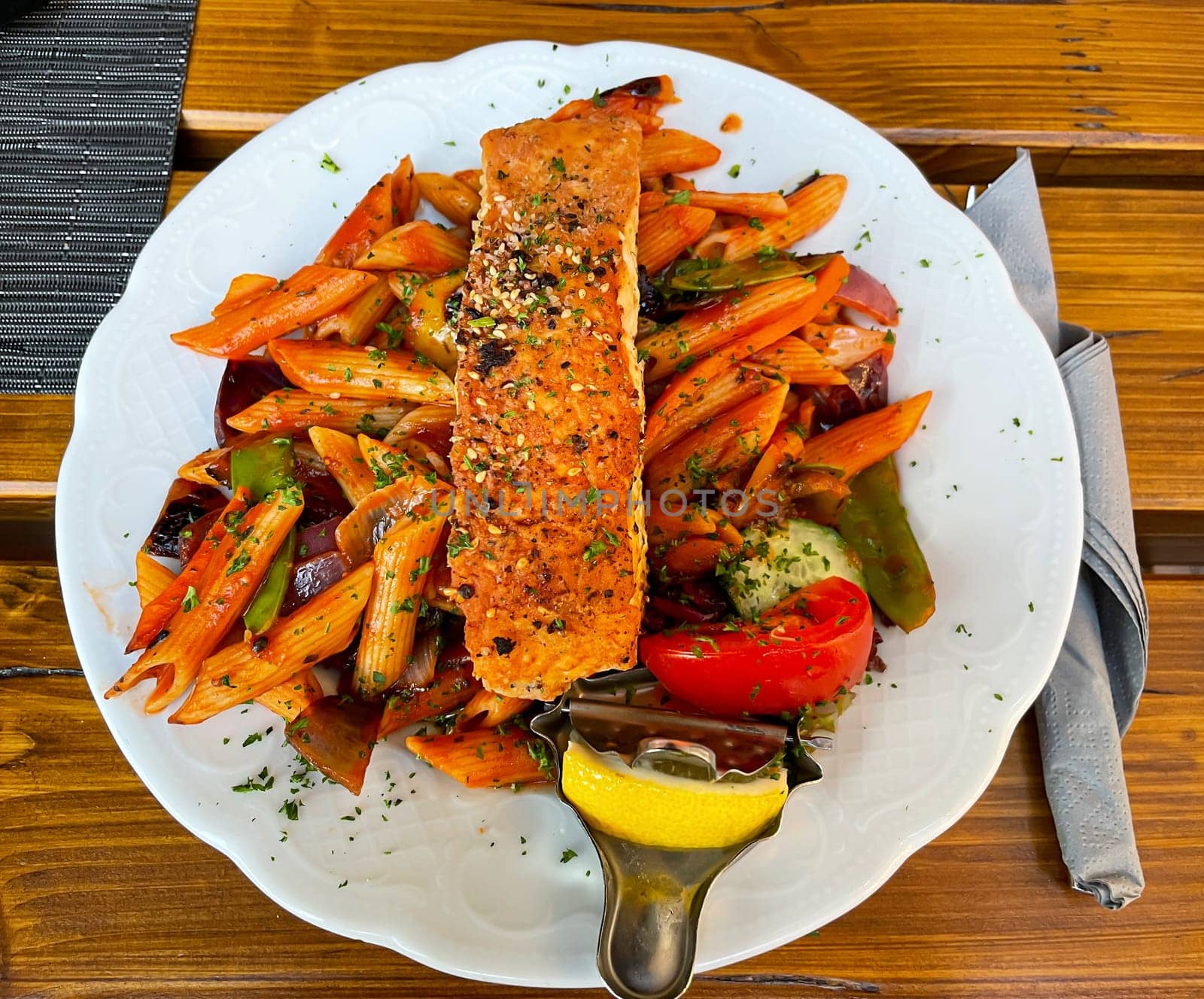 A plate of penne, pasta, vegetables and salmon.