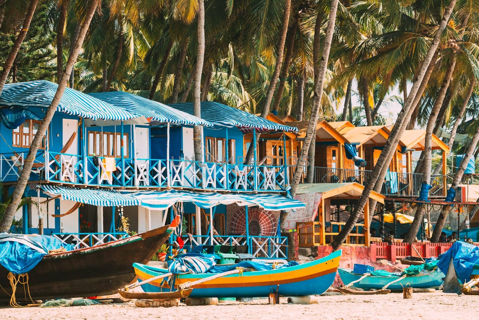 Canacona, Goa, India. Fishing Boat And Famous Painted Guest Houses On Palolem Beach Against Background Of Tall Palm Trees In Sunny Day.