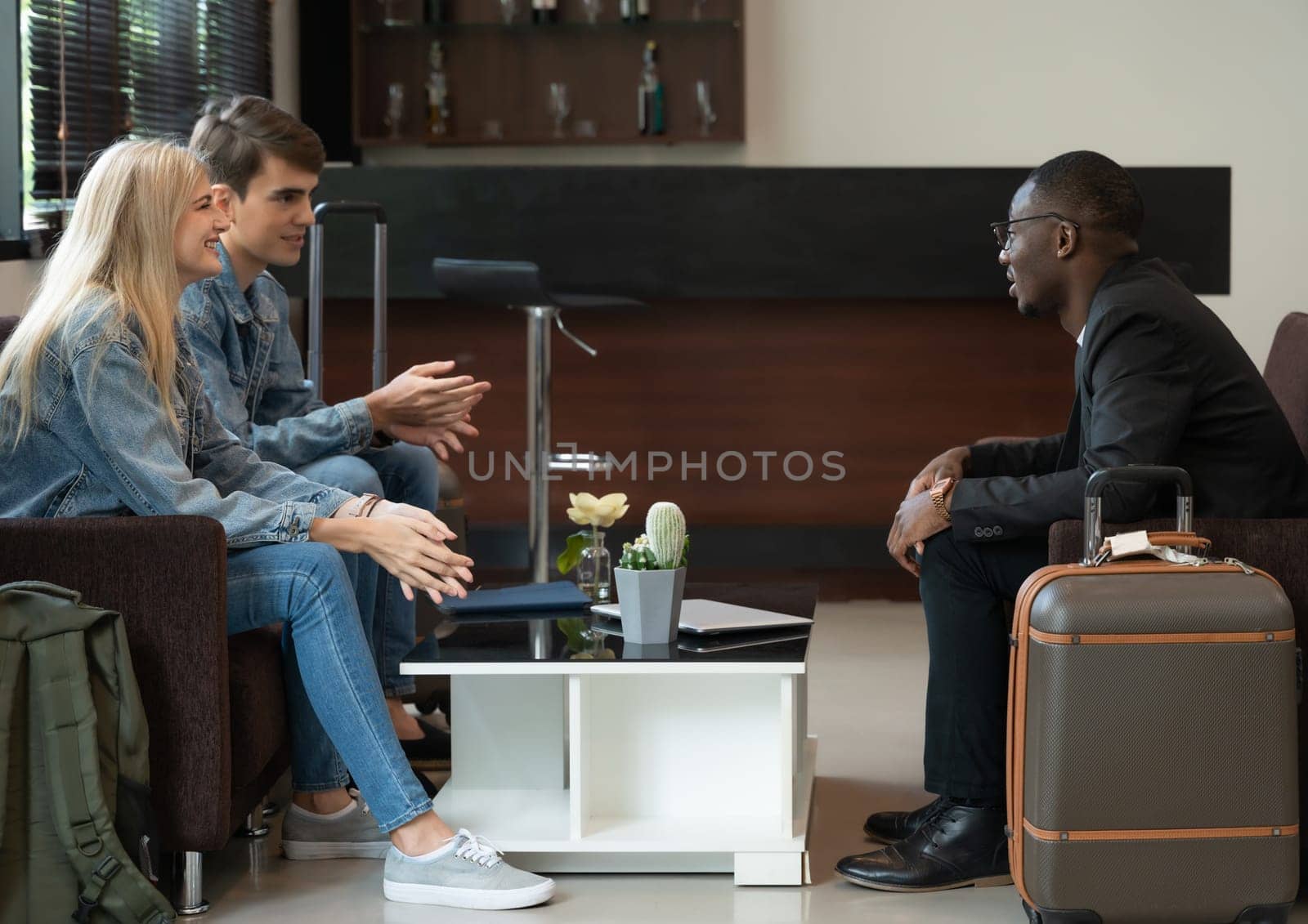 Businessman in black suit meeting and talking with couple travelers in blue jeans in airport lounge