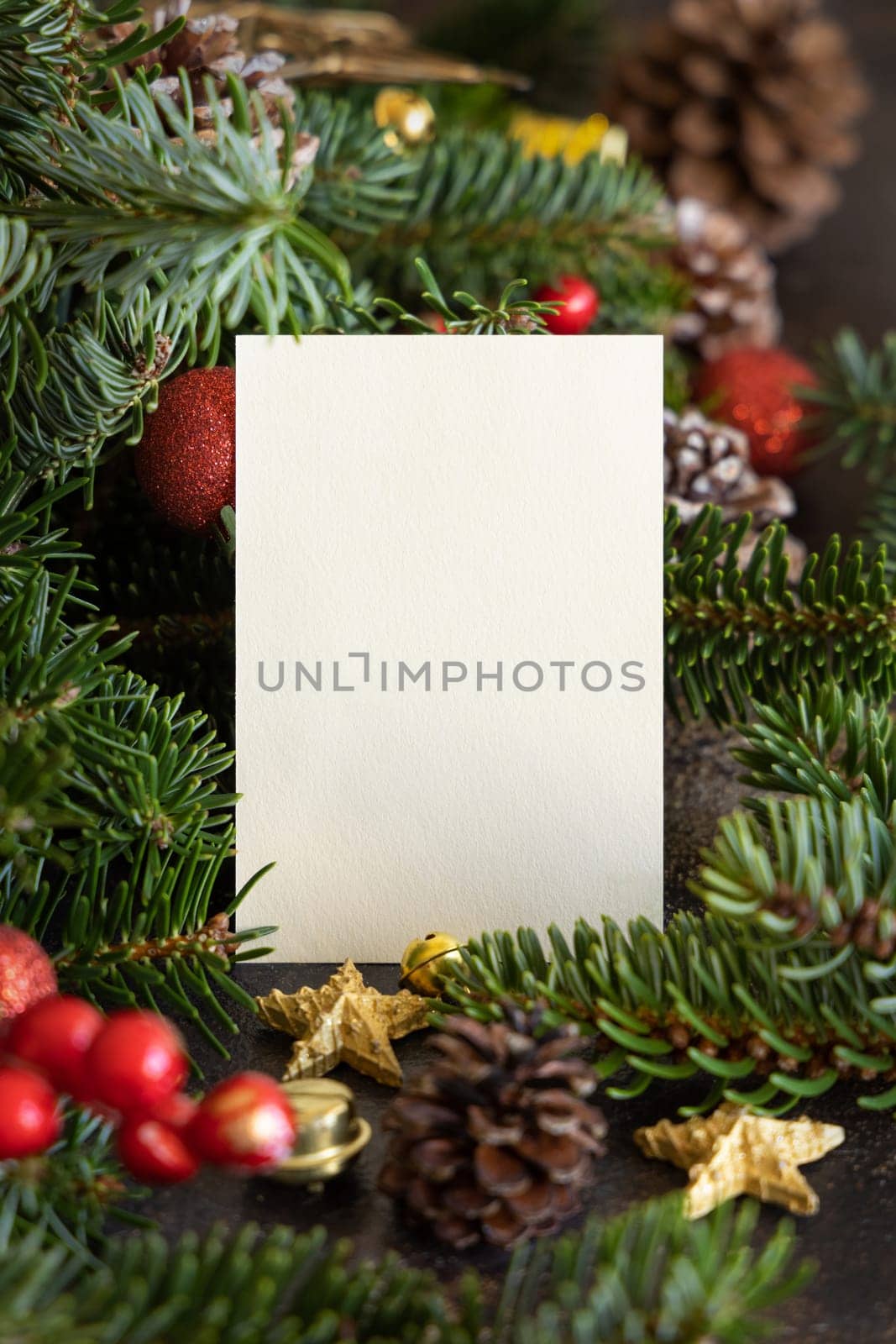Vertical blank card between decorations, fir branches and pine cones close up, mockup. Christmas or New Year greeting card template, Holiday or wedding stationery