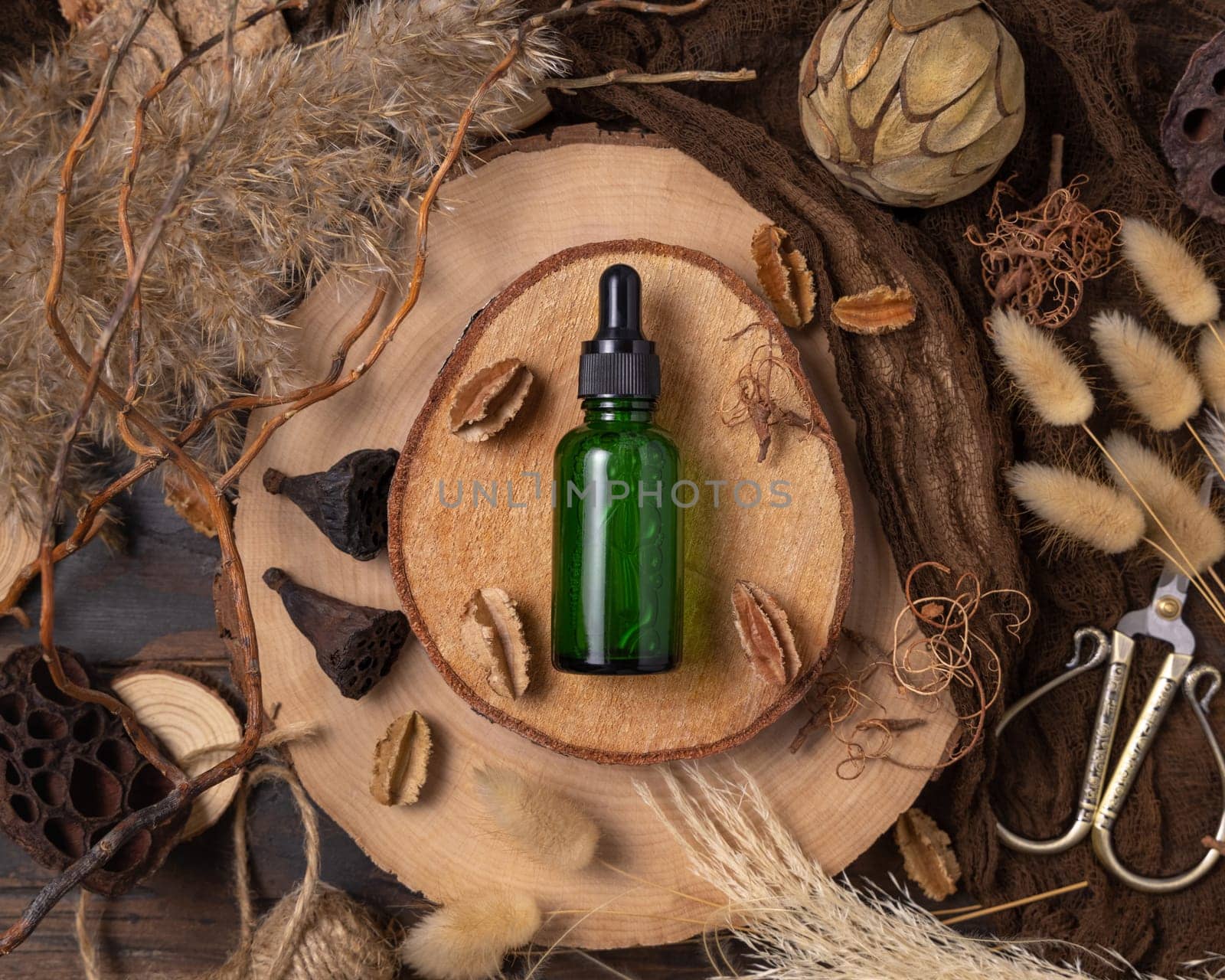 Green cosmetic dropper bottle with liquid on wood near natural boho decorations top view. Skincare beauty product, serum or essence. Bohemian eco friendly flat lay with dried leaves.