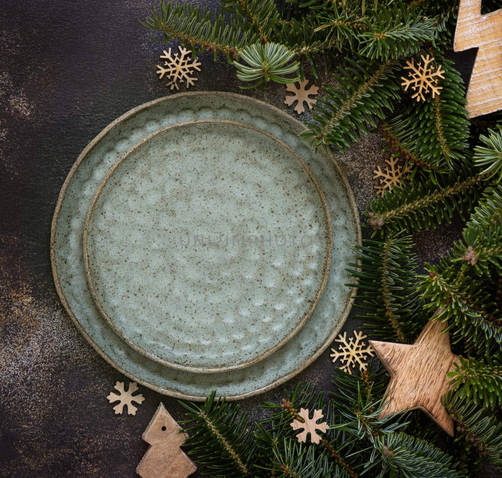 Festive table setting with fir tree branches and Rustic wooden decorations top view, copy space,. Christmas or New Year table place with green plates on dark table flat lay. Winter season, restaurant catering