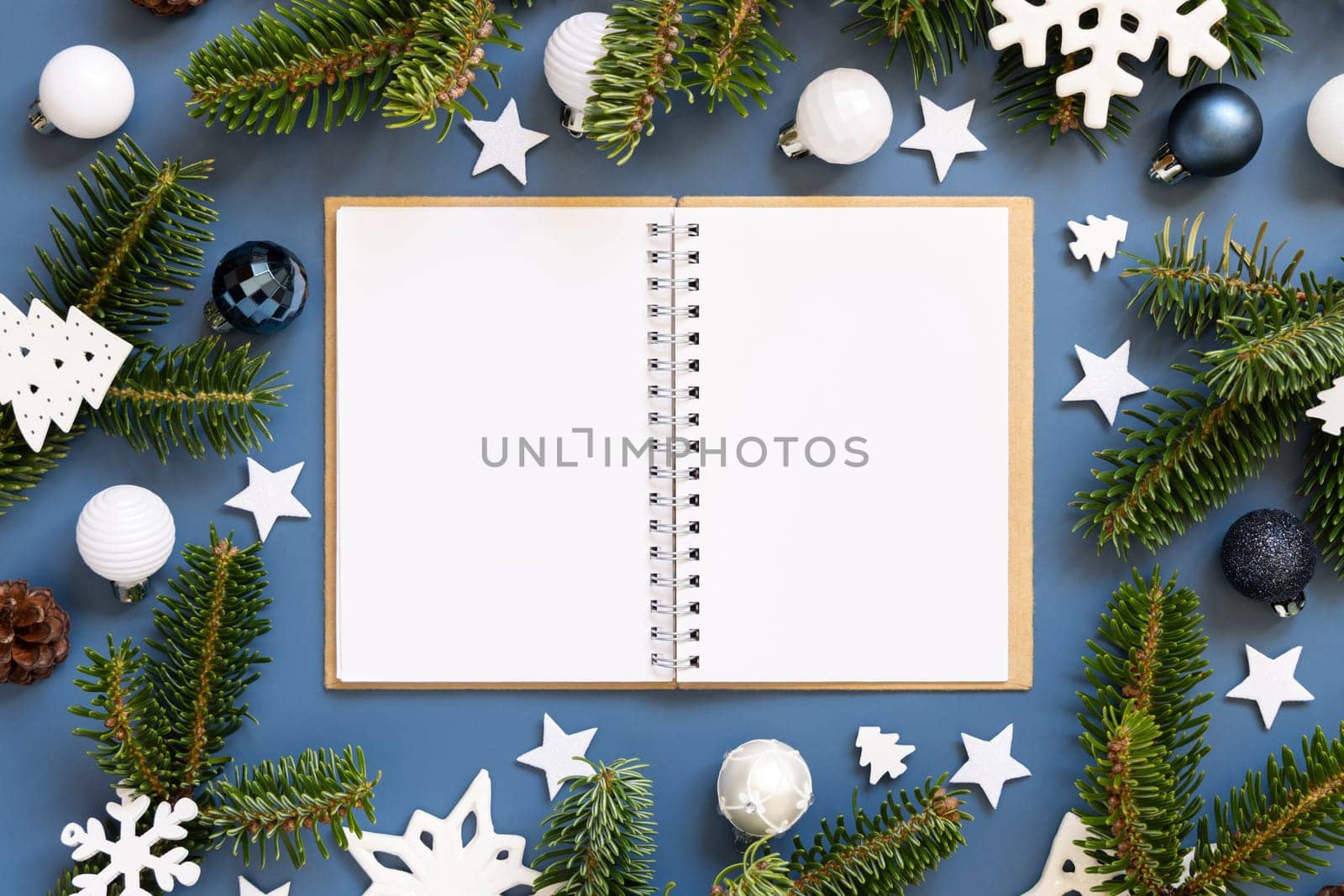 Blank open notepad on a blue background near white Christmas decorations and fir branches top view. New Year Textbook mockup flat lay, copy space. Planning and organizing concept