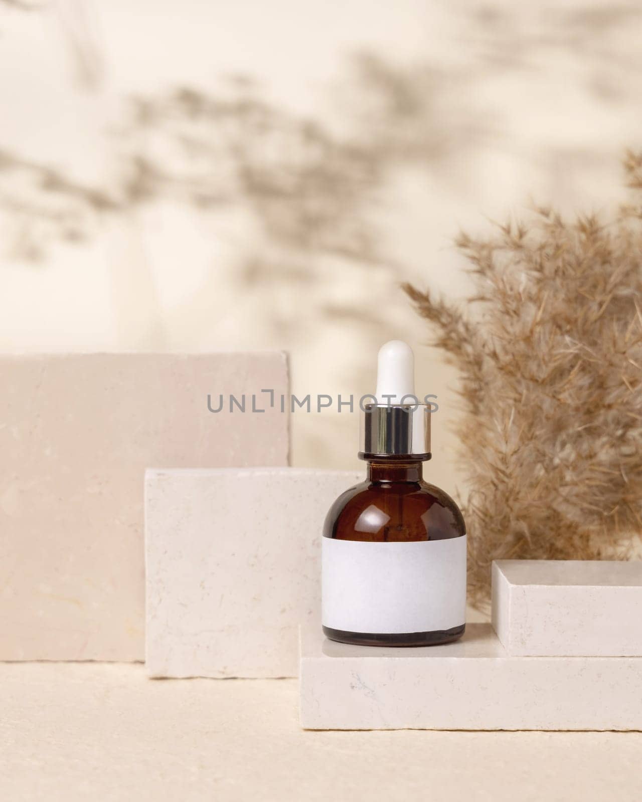 Brown dropper bottle with blank label on stones near pampas grass on light beige close up, packaging mockup. Skincare beauty product, lotion or cleanser. Natural eco friendly cosmetics