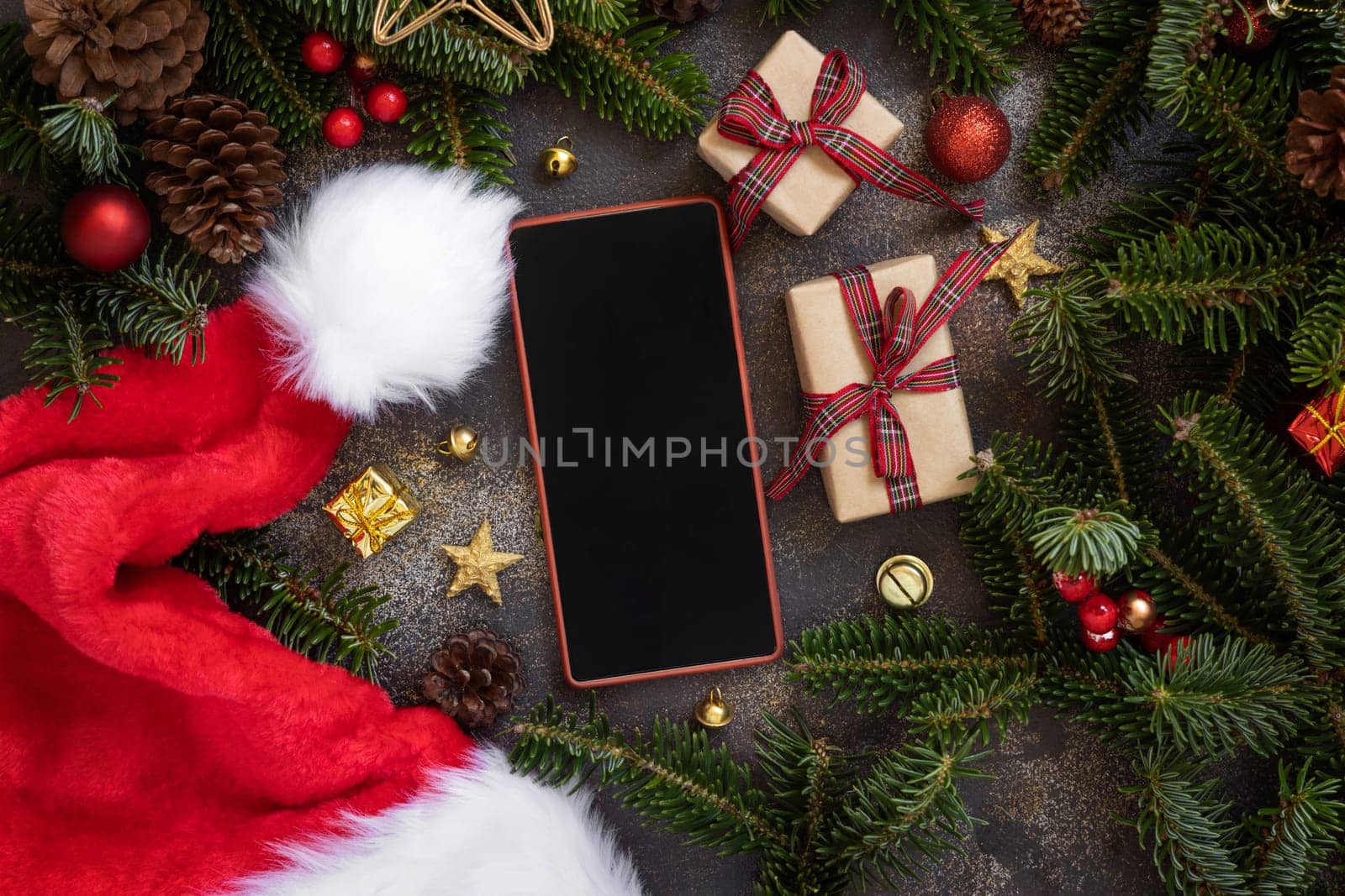 Mobile phone between Christmas decorations, wrapped gift boxes and green fir branches top view. Cell phone mockup with copy space. Christmas or New Year Holiday atmospheric flat lay
