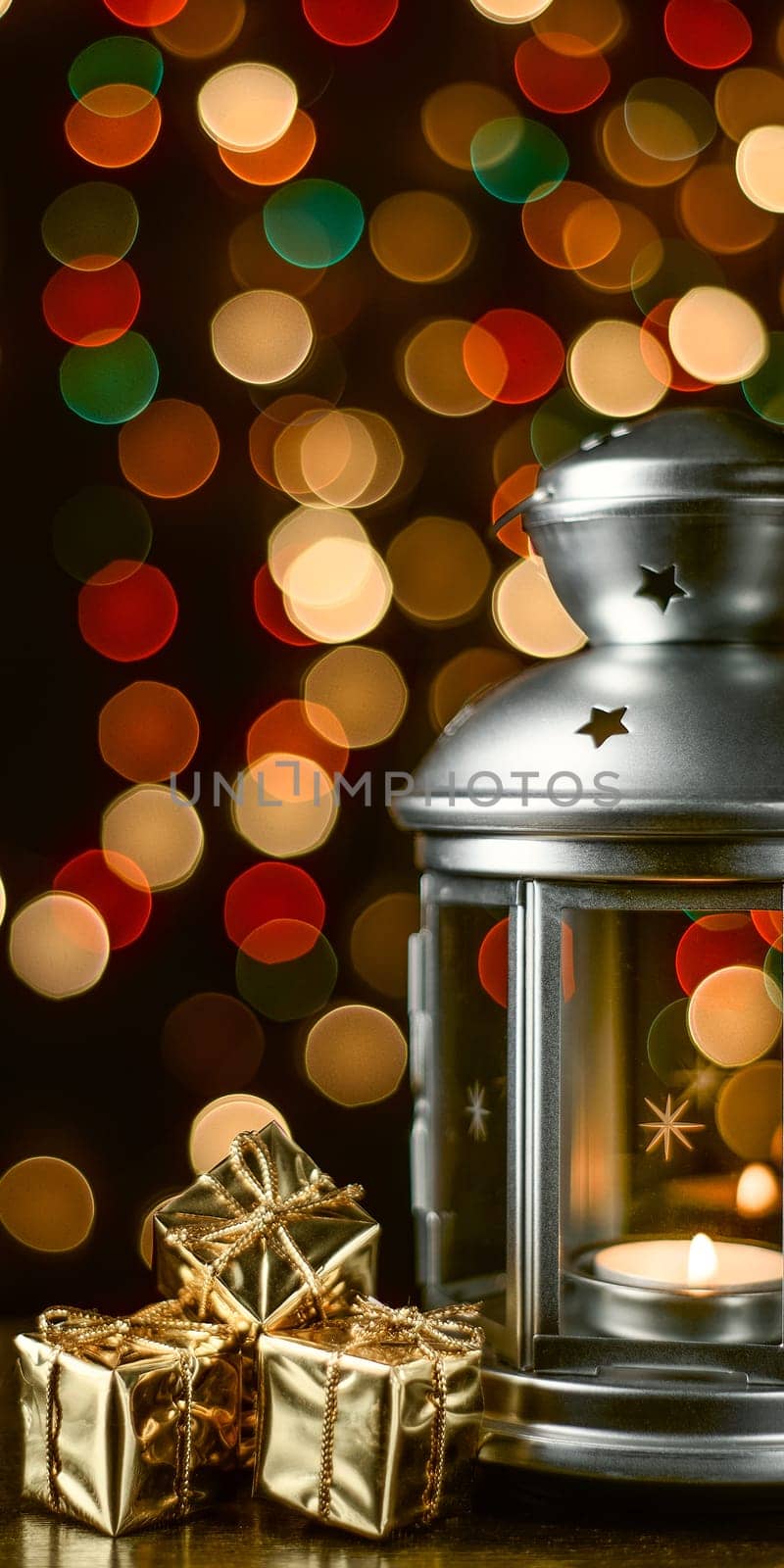 Christmas composition: a lantern with candles, bright shiny boxes with gifts, blurred bokeh lights in the background.