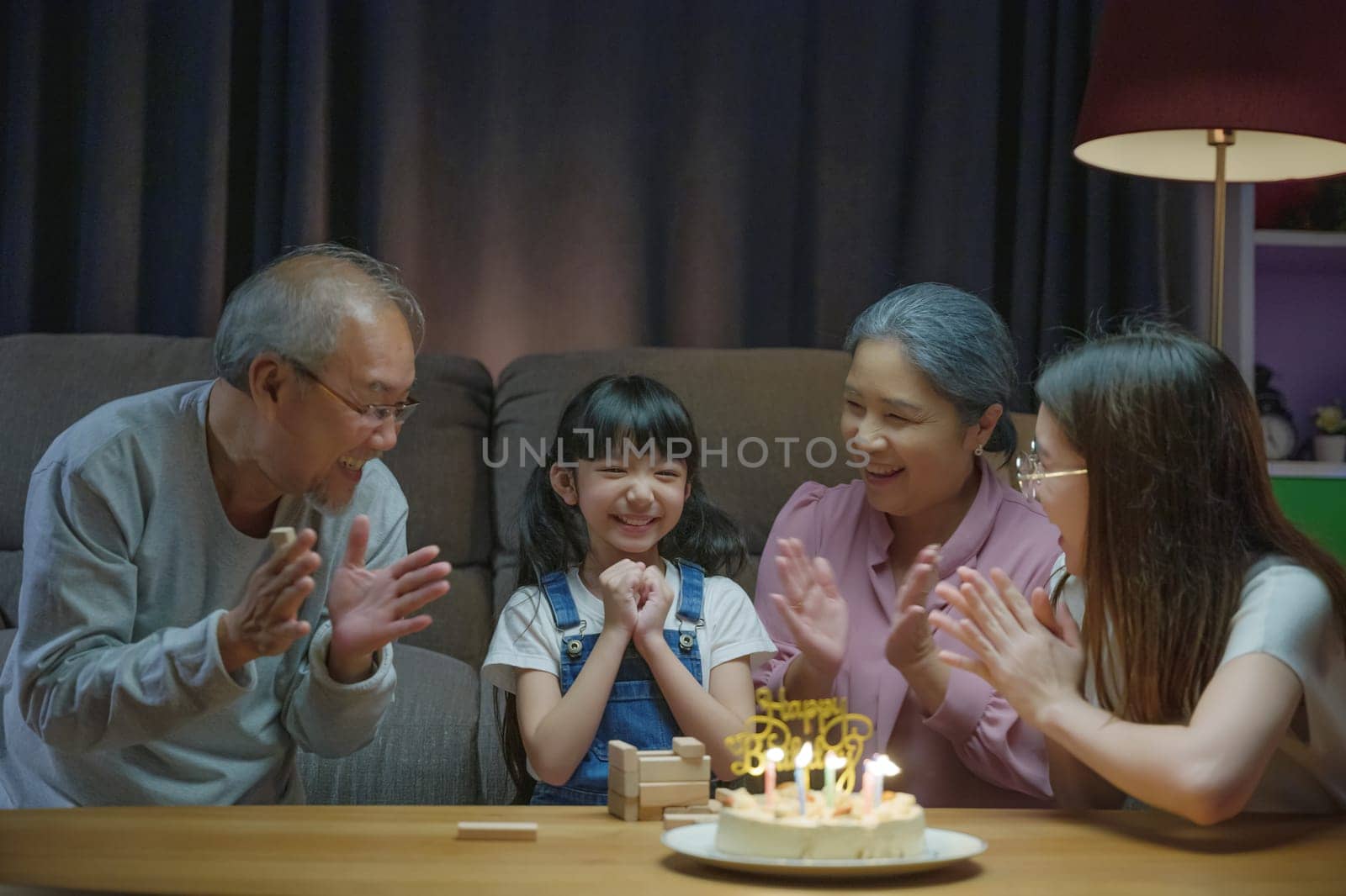 Birthday surprise. Happy Asian family grandparents and mother celebrating enjoy birthday party with cake of granddaughter at home in night time