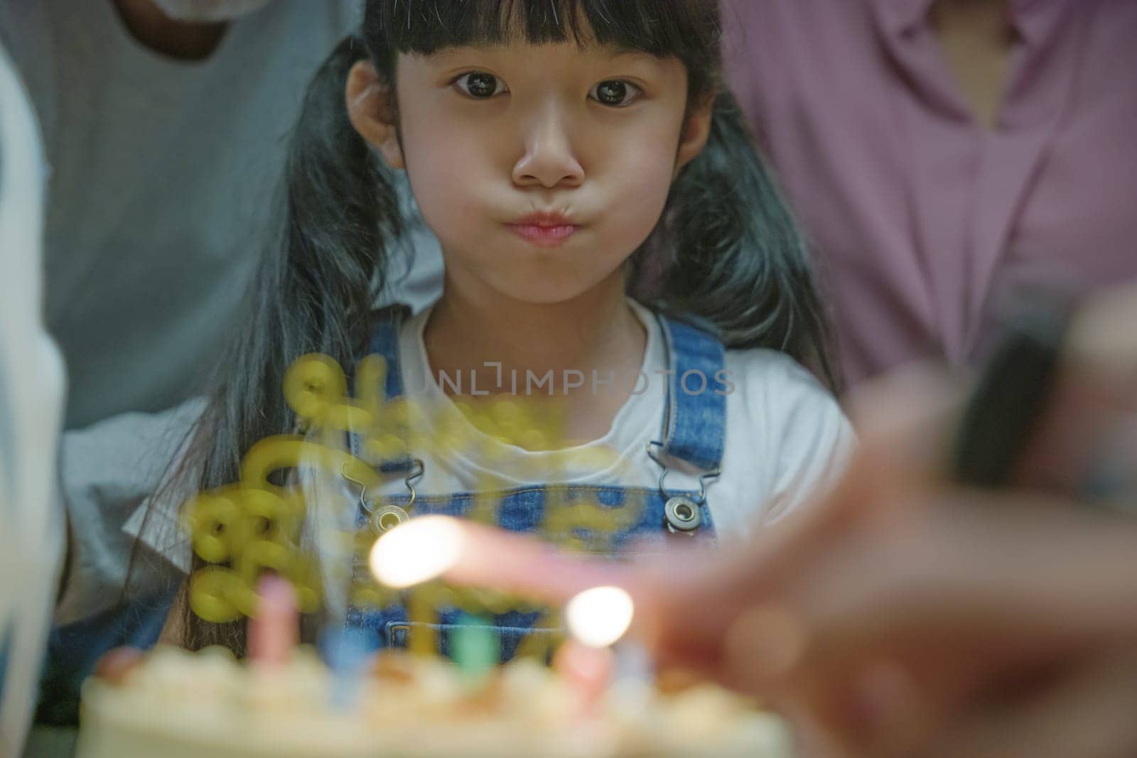 Happy Asian family grandparents and mother celebrating enjoy singing birthday song party with cake of granddaughter blowing candle at home in night time, Birthday surprise concept