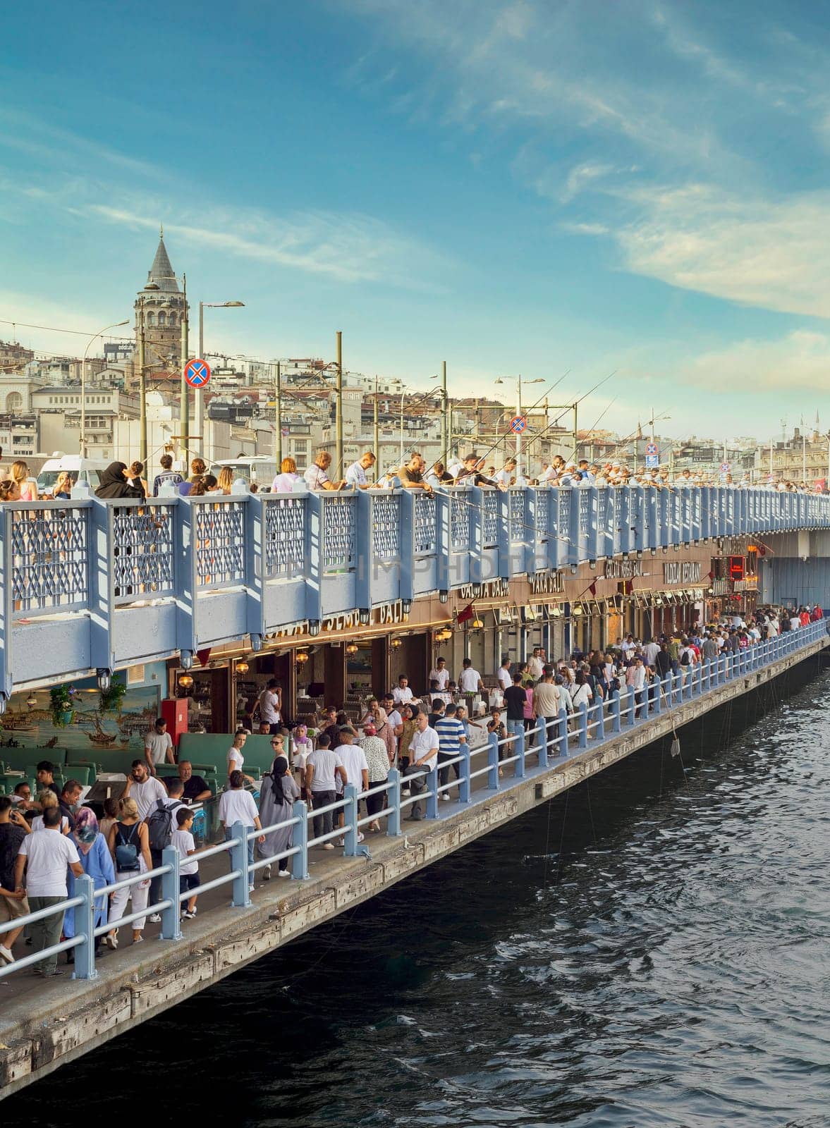 Istanbul, Turkey - August 30, 2022: Galata Bridge with traditional fish restaurants in the passage under the bridge, and crowds of People during Victory Day holiday with Galata Tower in the far end