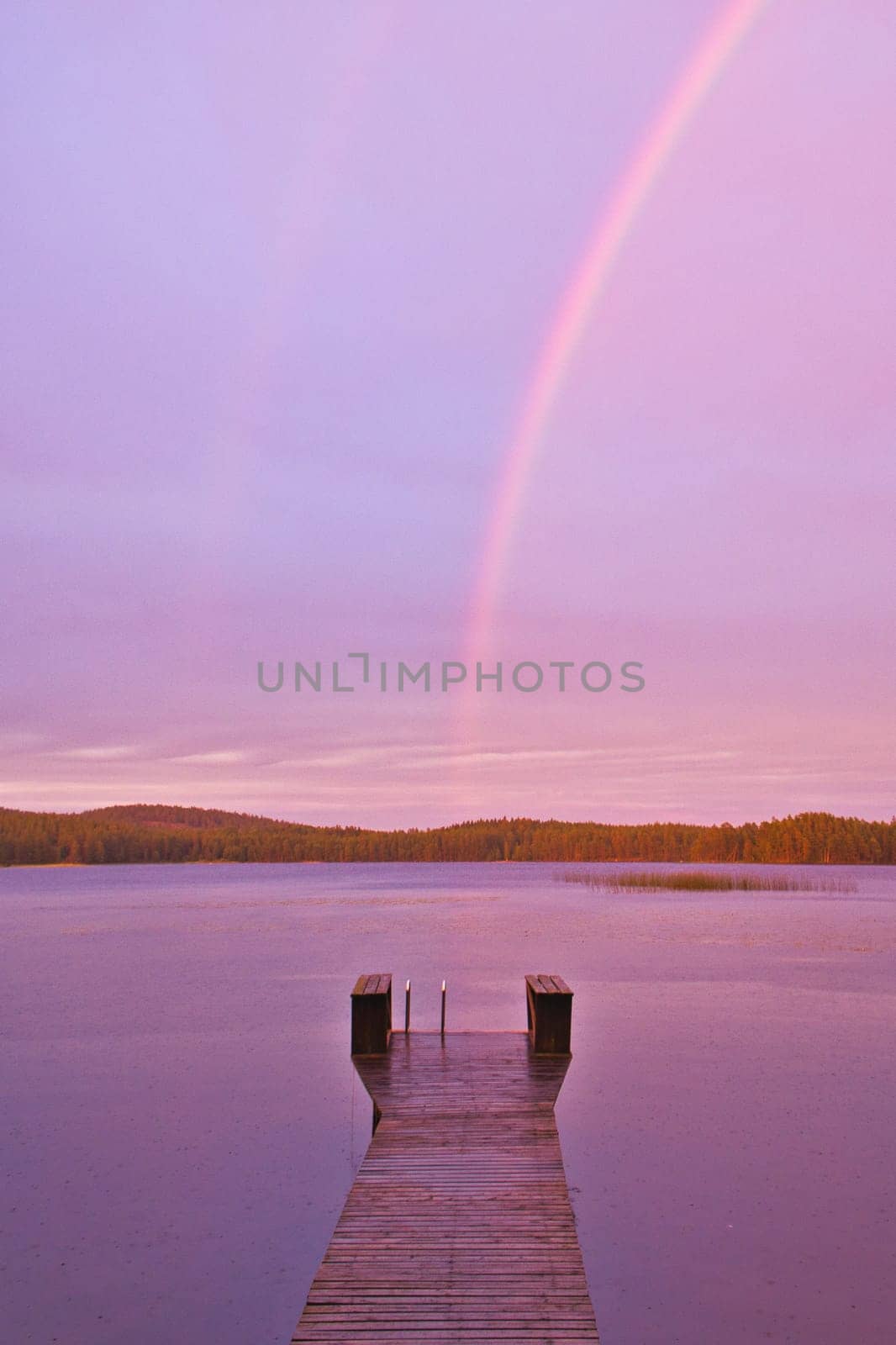 Footbridge reaching into the water at sunset with rainbow in the background when it rains. Nature photo from Sweden