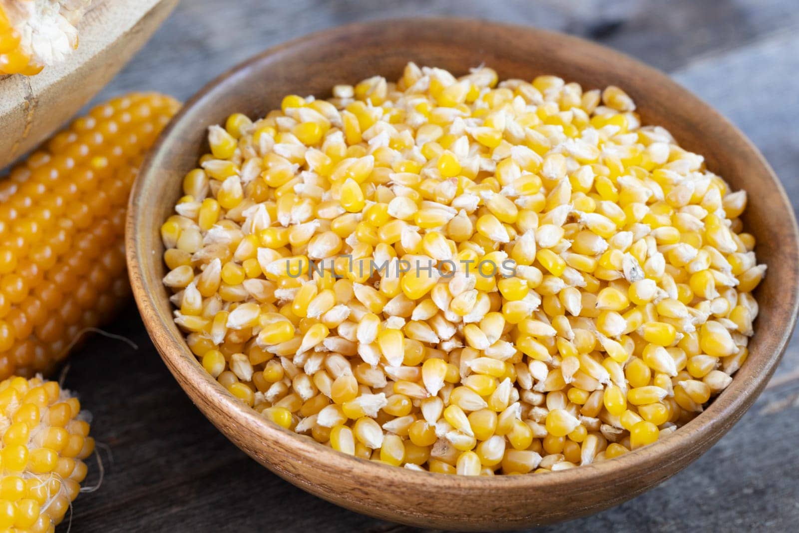 Popcorn kernels in a wooden bowl with popcorn on the cob