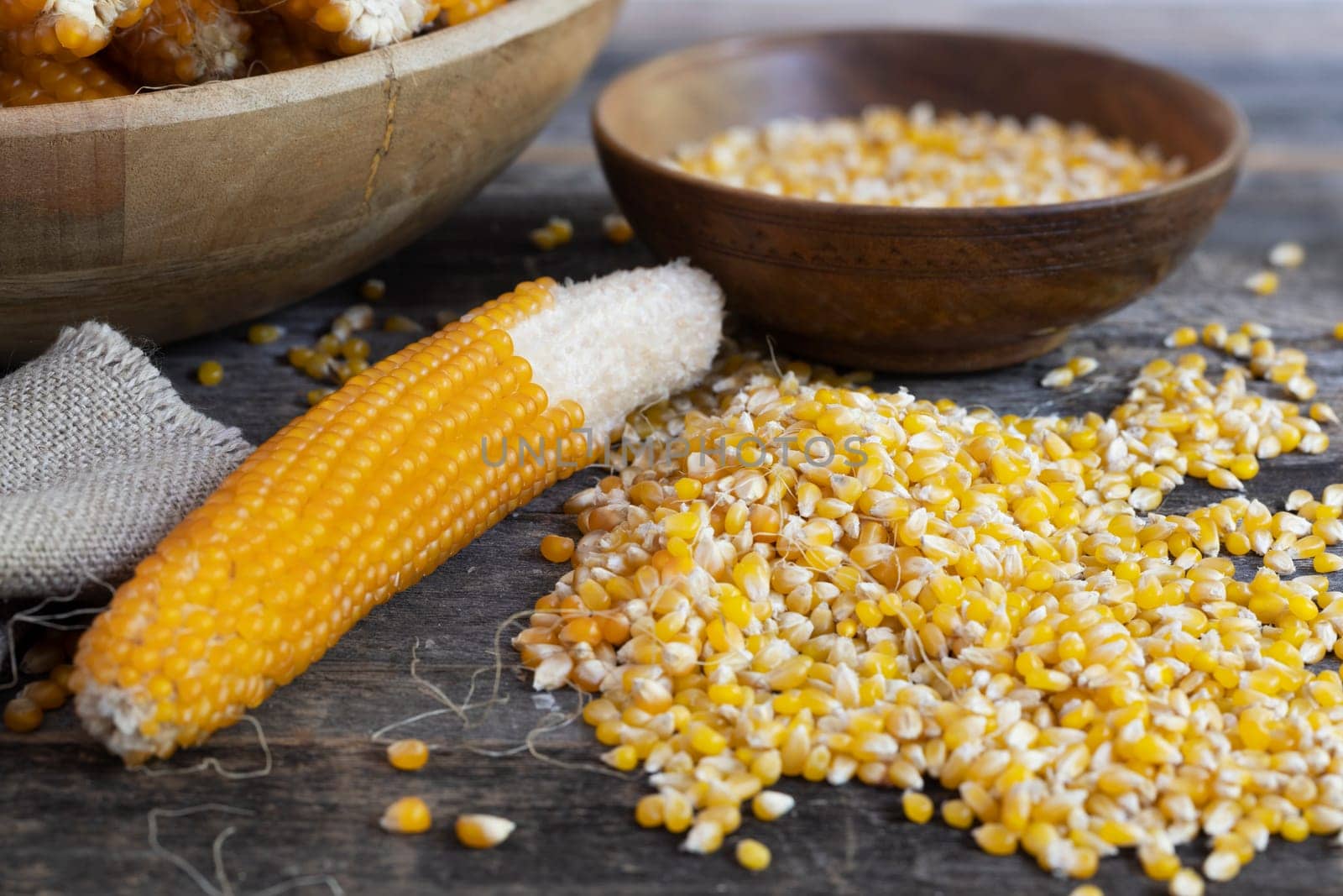 Harvesting popcorn from the cob with kernels and cobs in wooden bowls and on table.