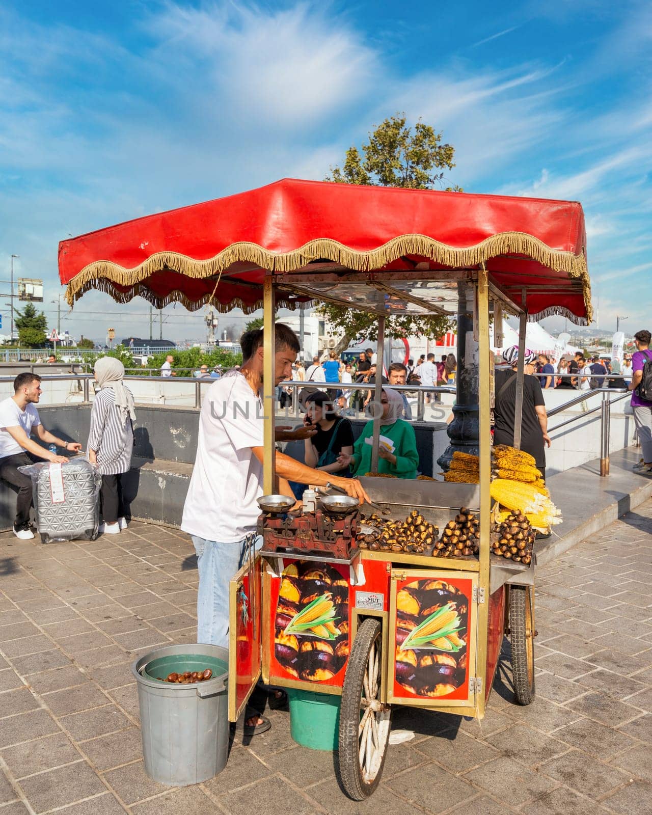 Istanbul, Turkey - August 30, 2022: Young man selling chestnut and corn on traditional Turkish fast food cart at Eminonu Piazza