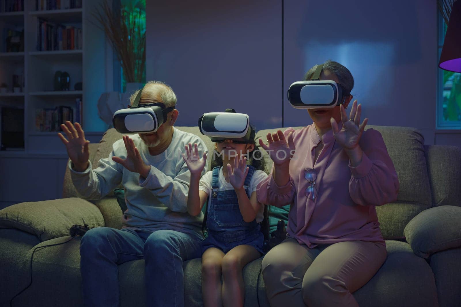 Asian granddaughter and grandparents playing together exciting interesting video games using virtual reality headsets living room at home, elderly with child play VR video game, family entertainment
