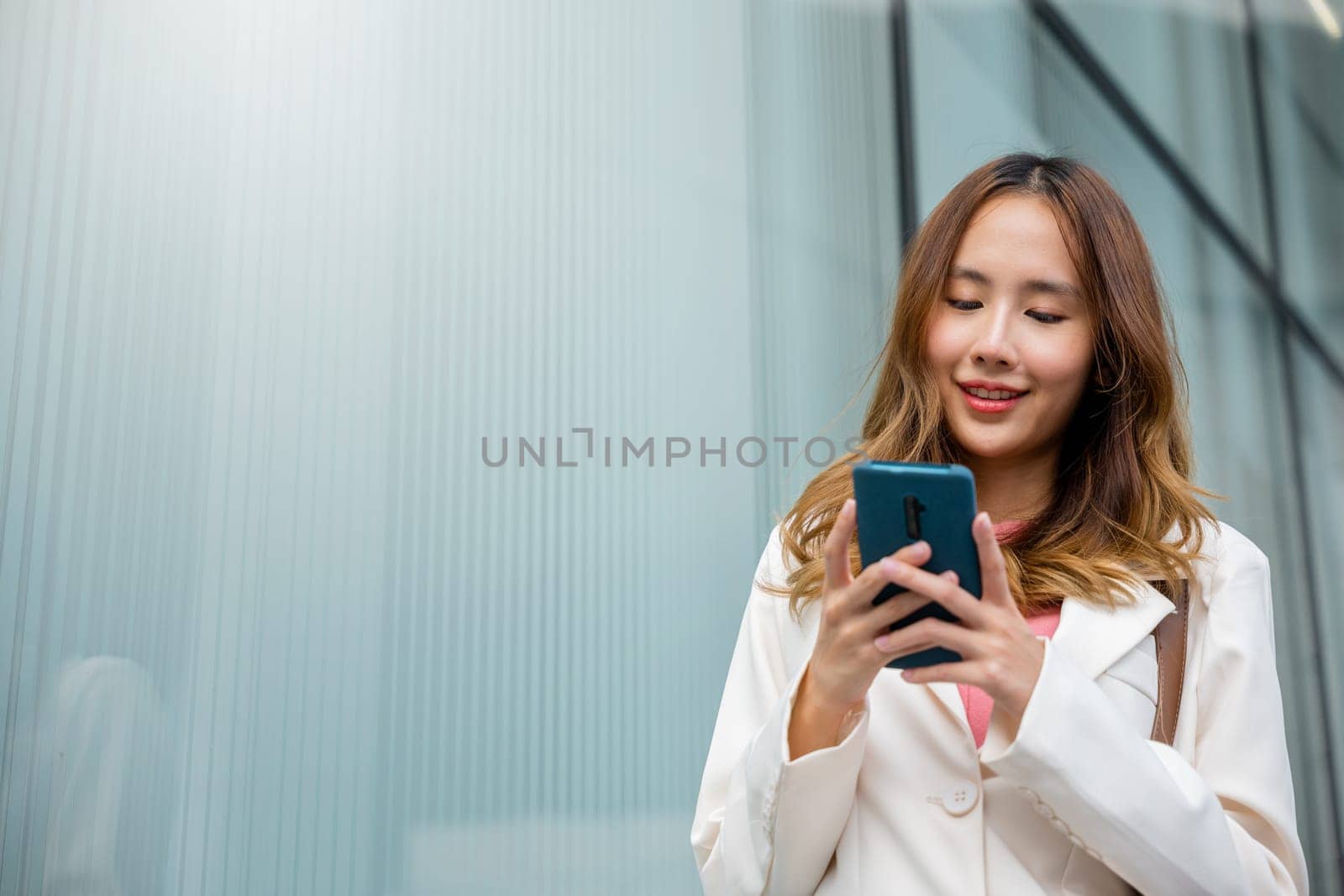 Asian businesswoman texting smartphone commuting work she walking near her office building in morning, Beautiful business woman smiling hold mobile phone outdoor walking on city street urban