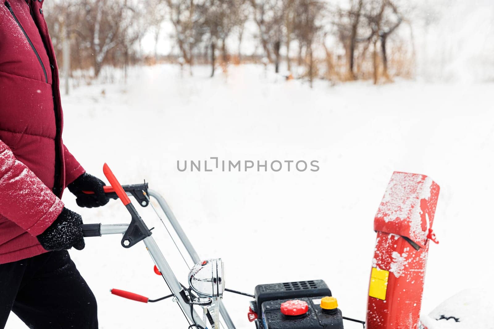 Detail of portable red snow blower powered by gasoline in action. Man outdoor using snowblower machine after snowstorm. Snow removal, thrower assistant in winter. Guy blowing snow during blizzard