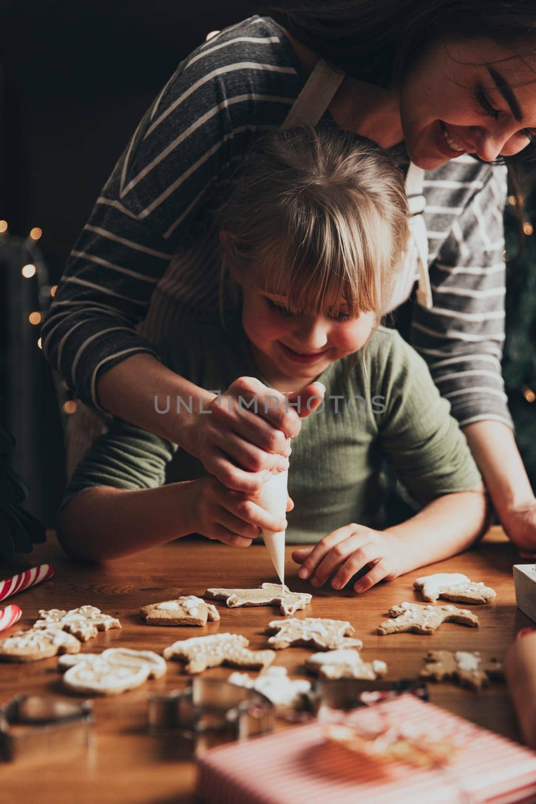Christmas, New Year gingerbread cooking, making, decorating freshly baked cookies with icing and mastic. Mommy and child, authentic lovely moments. Mom helping cute little daughter to decorate cookie