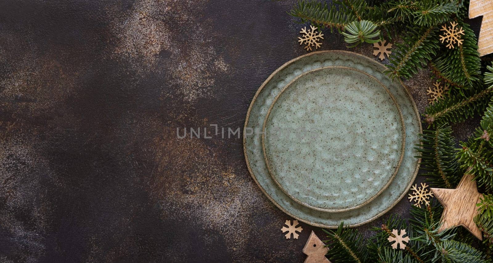 Festive table setting with fir tree branches and Rustic wooden decorations top view, copy space,. Christmas or New Year table place with green plates on dark table flat lay. Winter season, restaurant catering