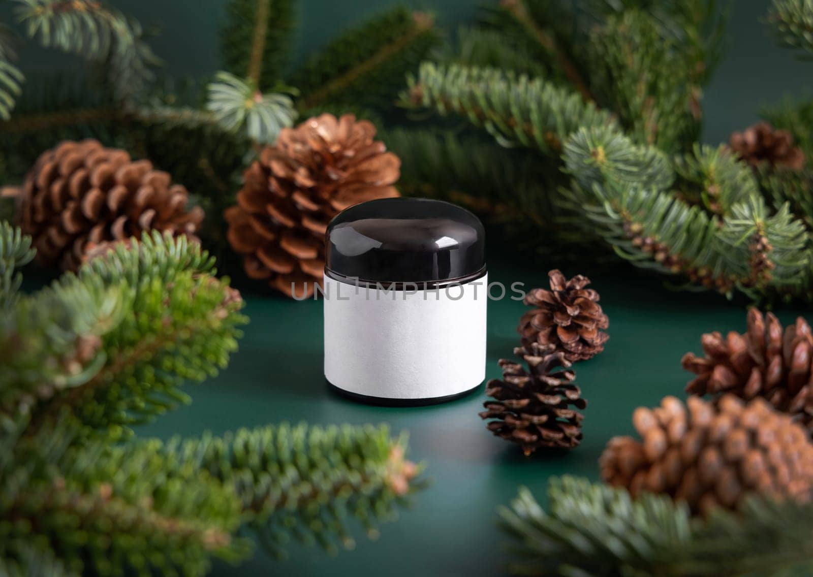 Brown glass jar near fir branches and pine cones on dark green close up. Brand packaging mockup. Skincare beauty product, cream or serum. Healthcare natural cosmetics concept