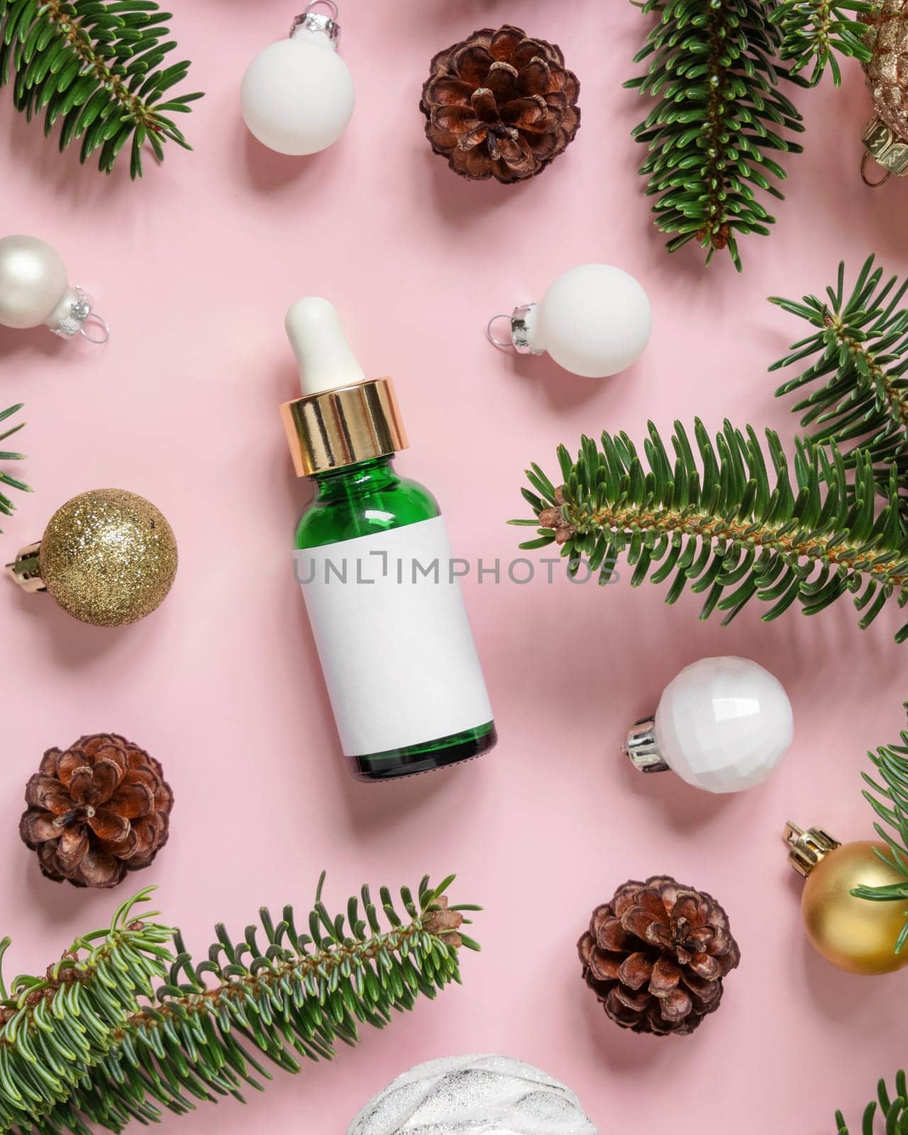Green Dropper Bottle near Christmas decorations, fir branches and pine cones on pink top view. Holiday brand packaging mockup. Skincare beauty product, cream or serum. Healthcare natural cosmetics